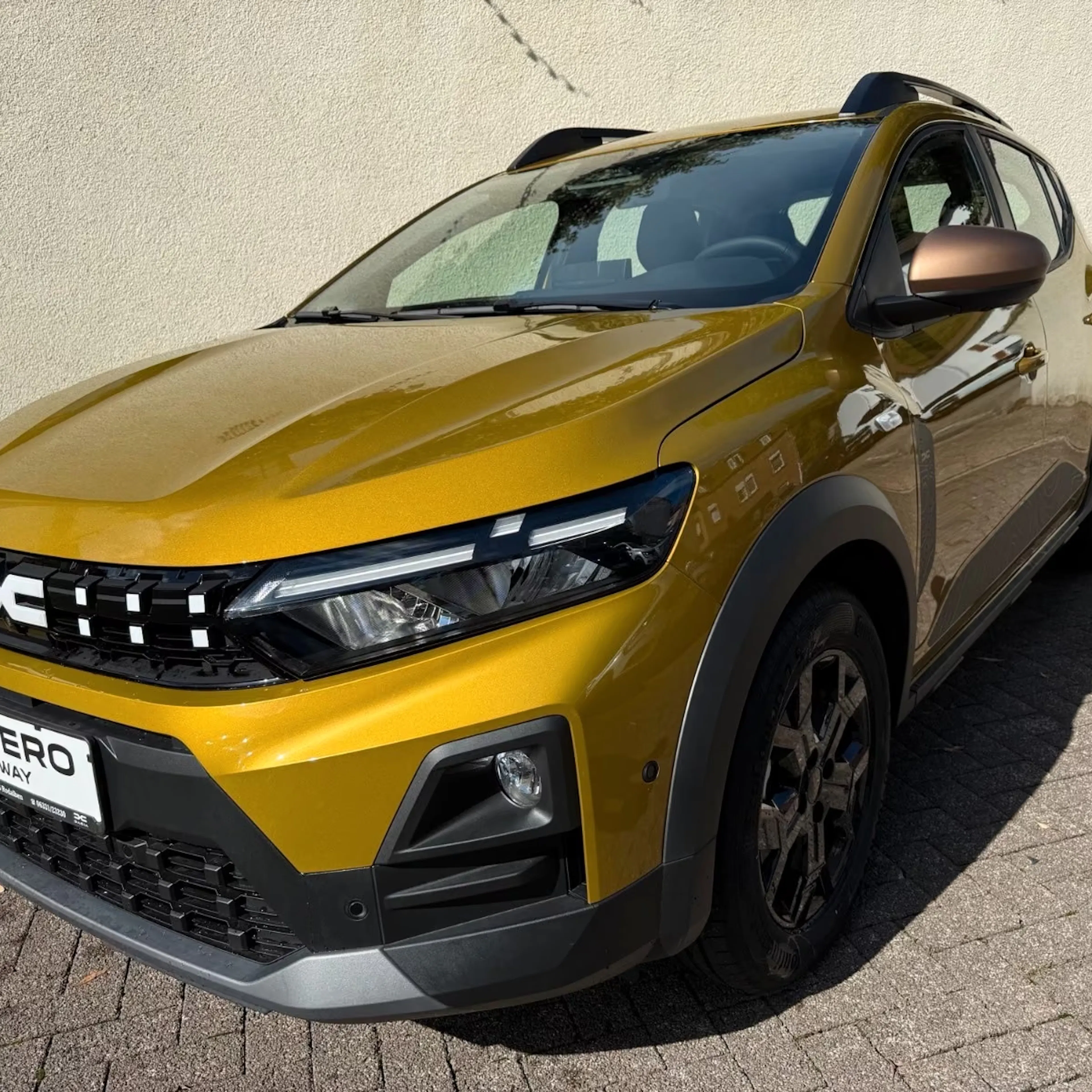 Ein goldgelber Dacia Sandero Stepway Hybrid steht auf einer gepflasterten Fläche.