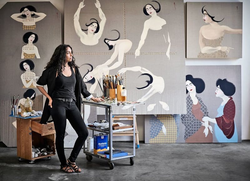 LA-based, Iraq-born artist Hayv Kahraman standing in front of artwork and painting tools and supplies.
