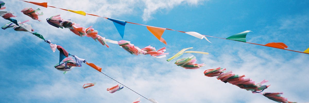 Three colorful lines of streamers and flags in front of a partially cloudy sky