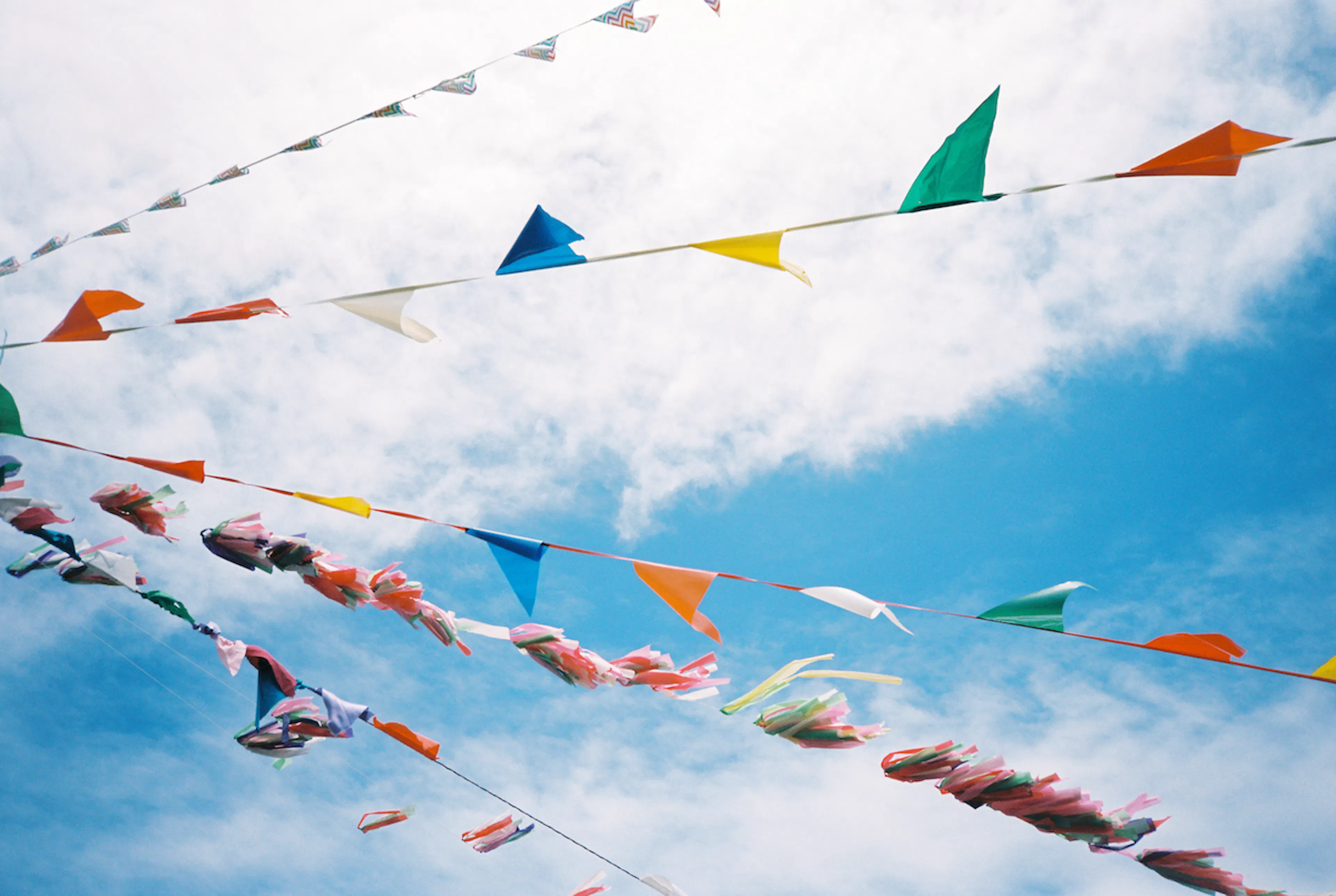 Three colorful lines of streamers and flags in front of a partially cloudy sky