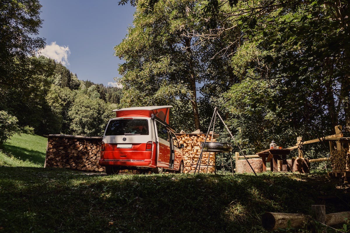 A red travel van parked in a beautiful green space.