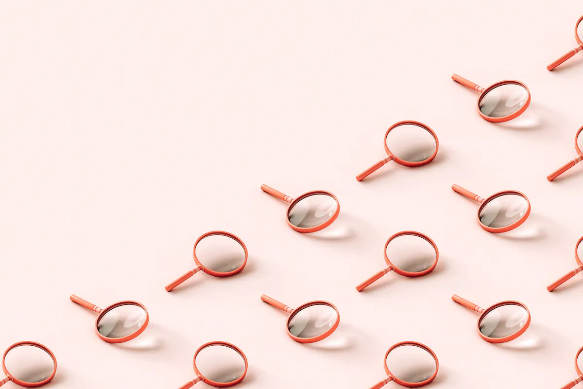 Pink 3D magnifying glasses covering half the frame diagonally, pale pink background.
