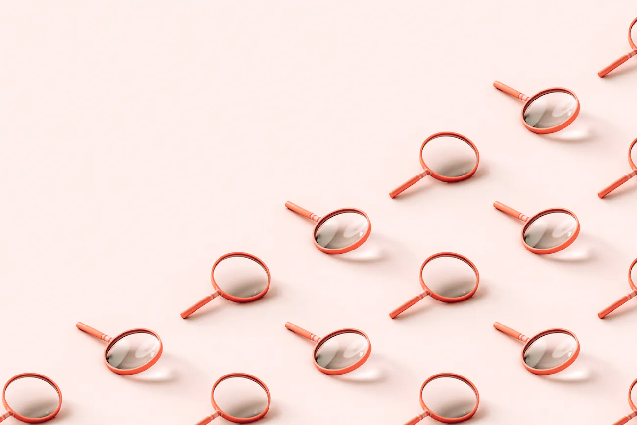 Pink 3D magnifying glasses covering half the frame diagonally, pale pink background.