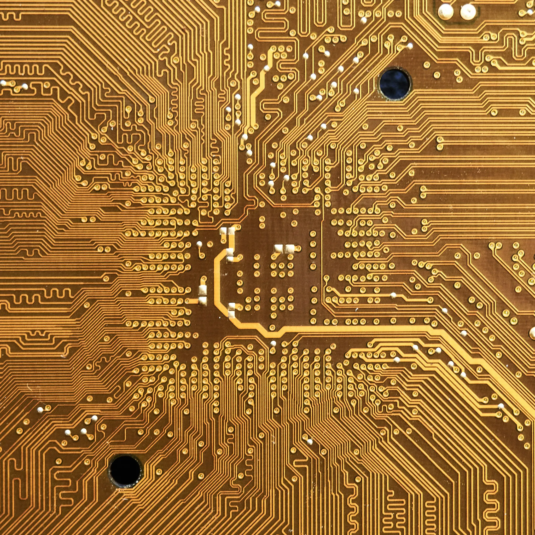 A brown printed circuit board with intricate gold conductive pathways and small solder points