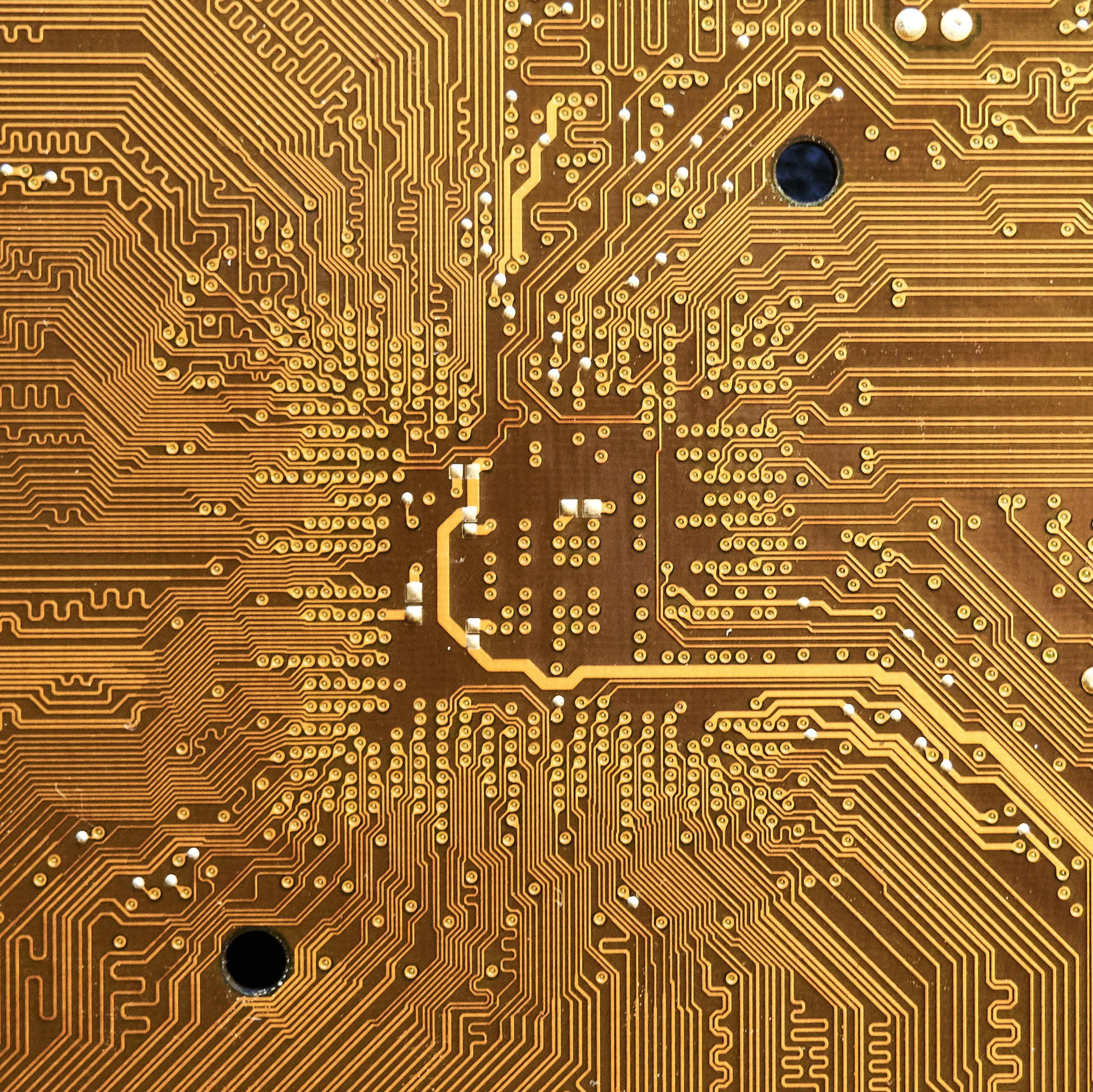 A brown printed circuit board with intricate gold conductive pathways and small solder points