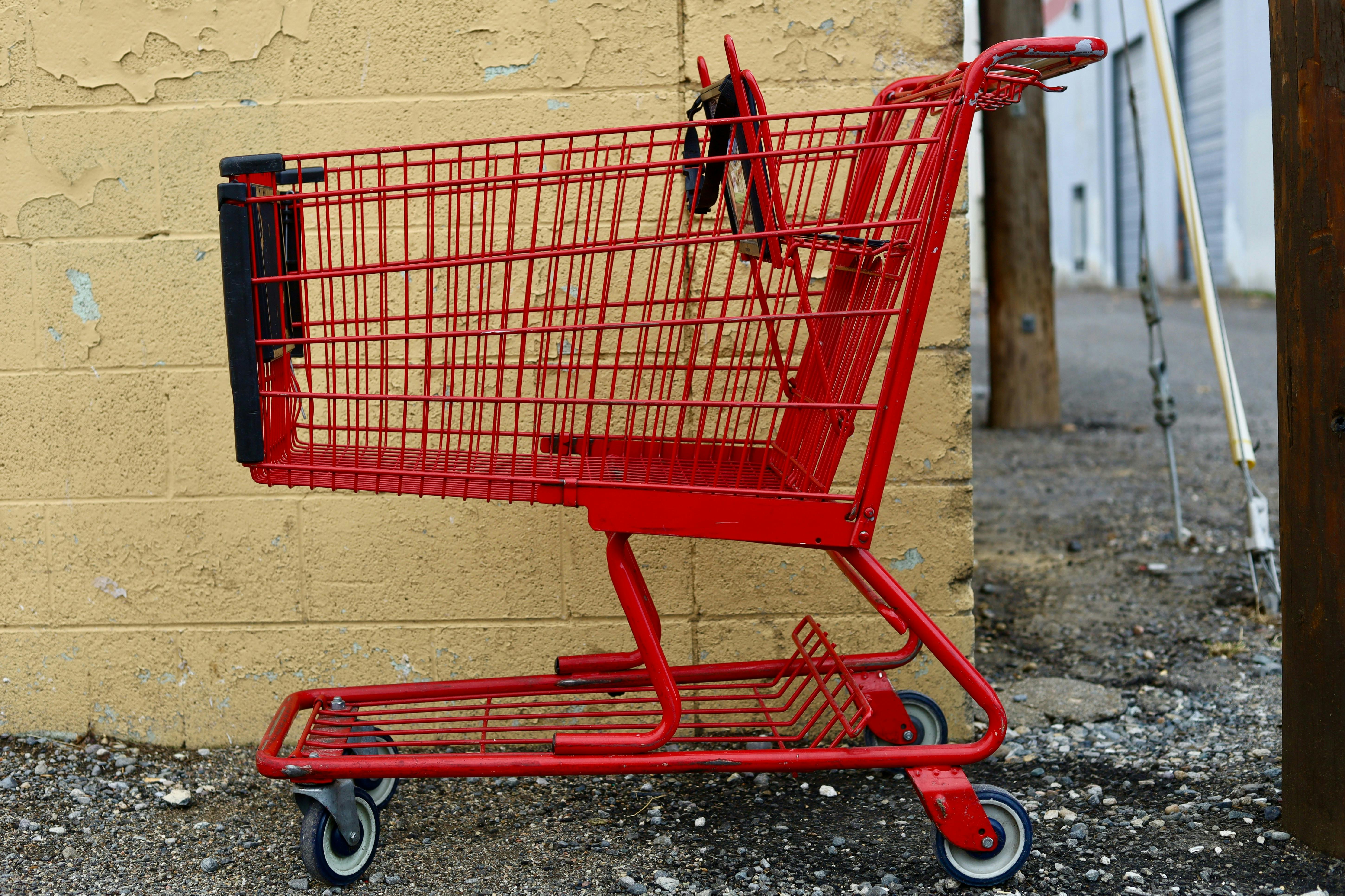 A red shopping cart in front of a brick wall with chipping yellow paint.