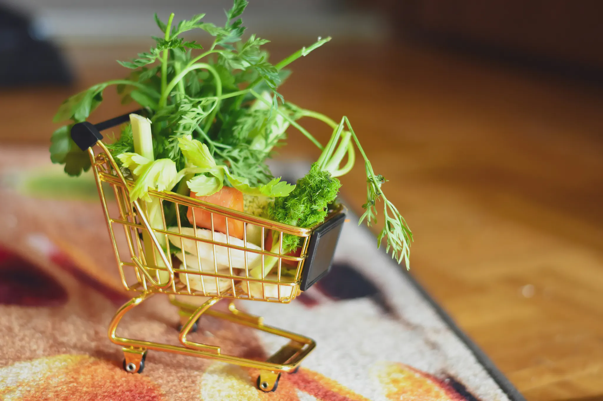 A small brass shopping cart overflowing with small vegetable parts on a soft rug, with some wooden floor visible next to the rug.