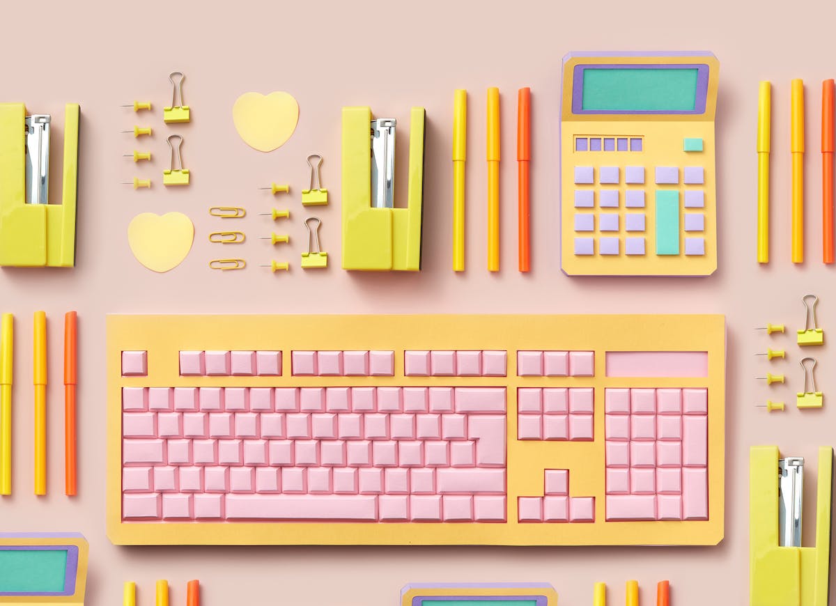 Colorful office supplies, some of which are made of paper. There is a row with two heart-shaped post-it notes, multiple yellow paper clips and thumbtacks, a yellow stapler on its side, three capped markers, and a calculator made out of paper. Below these, there is a computer keyboard, also made out of paper.
