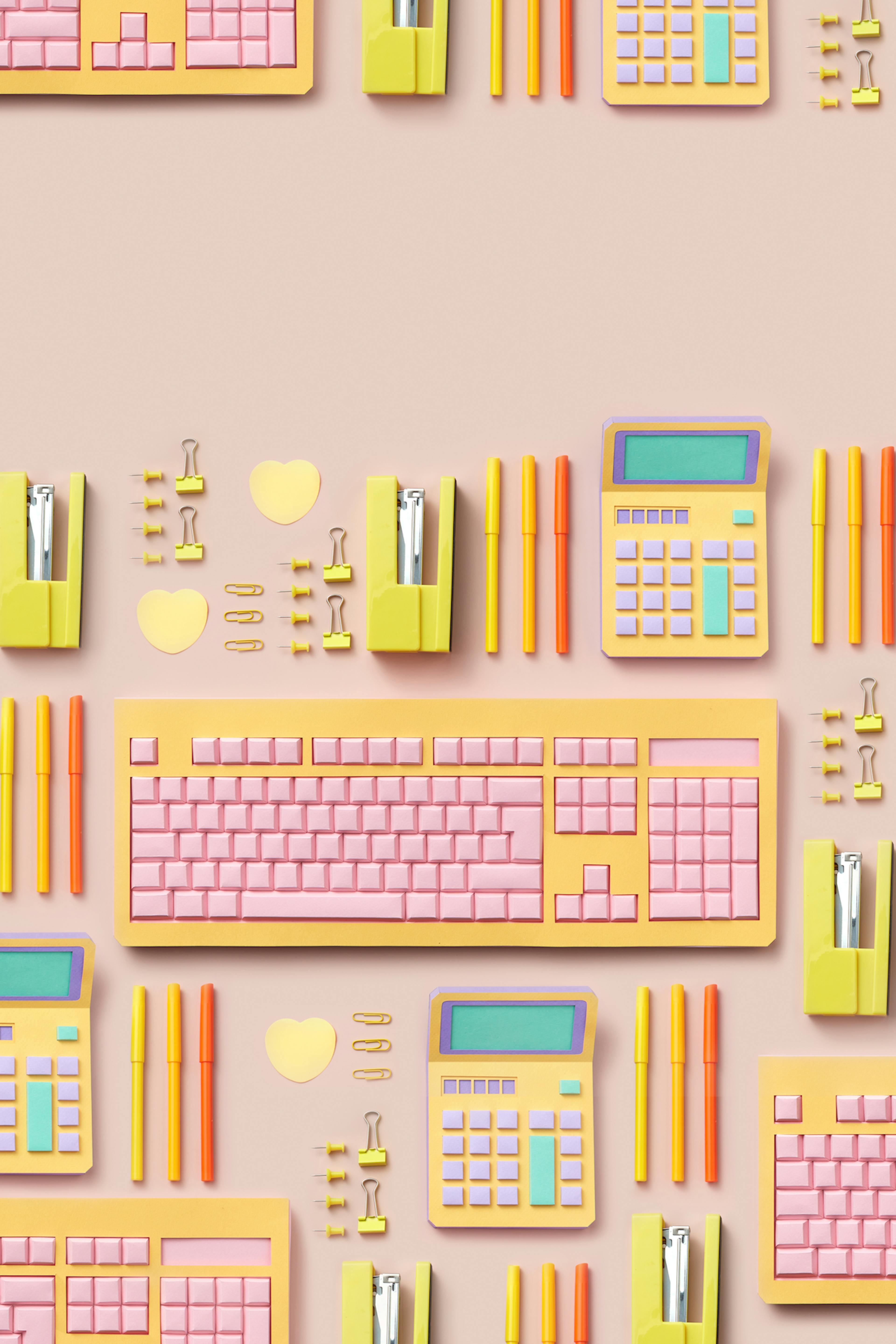 Colorful office supplies, some of which are made of paper. There is a row with two heart-shaped post-it notes, multiple yellow paper clips and thumbtacks, a yellow stapler on its side, three capped markers, and a calculator made out of paper. Below these, there is a computer keyboard, also made out of paper.