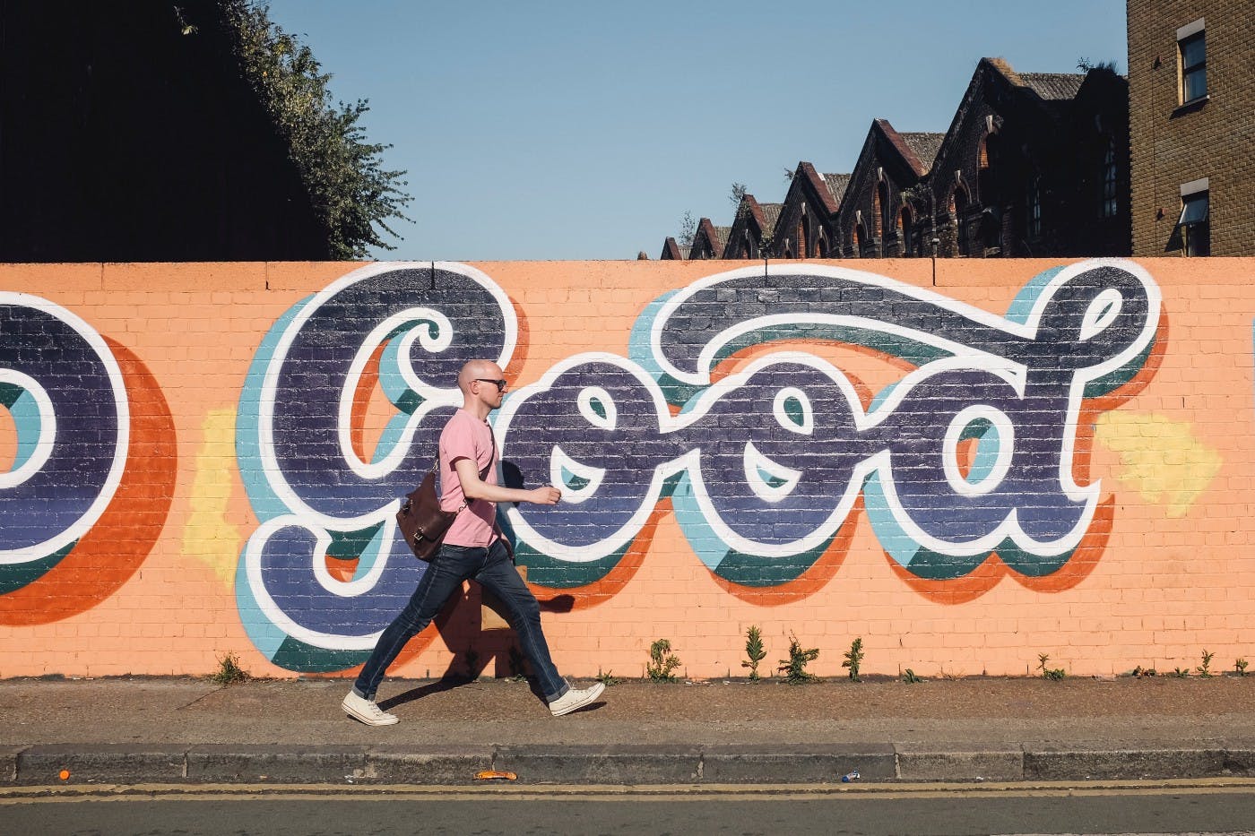 A man walking next to a wall that has a graffiti spelling Good. Photo by Volkan Olmez on Unsplash.