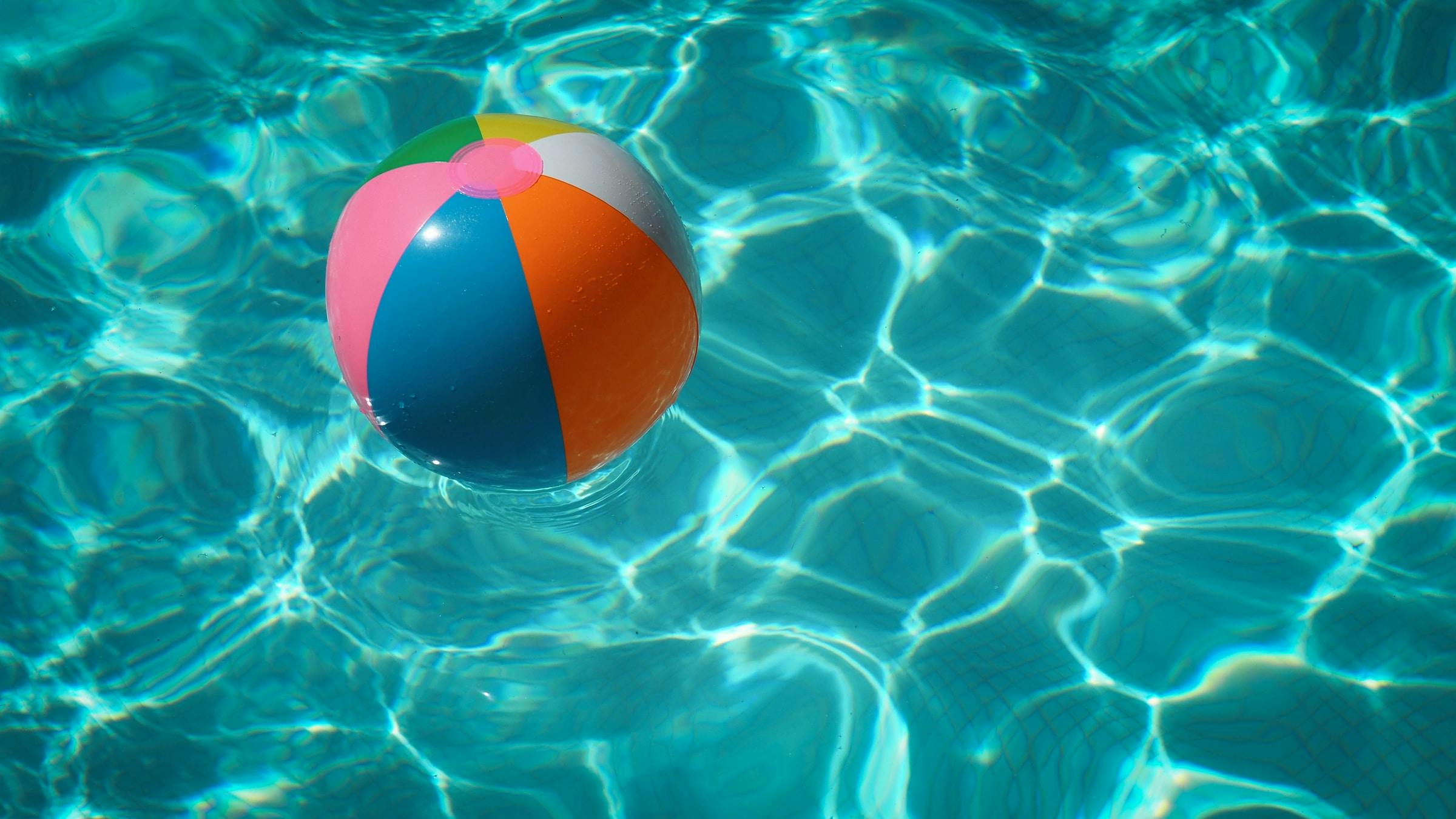 A beach ball floating in a pool with tiles at the bottom.