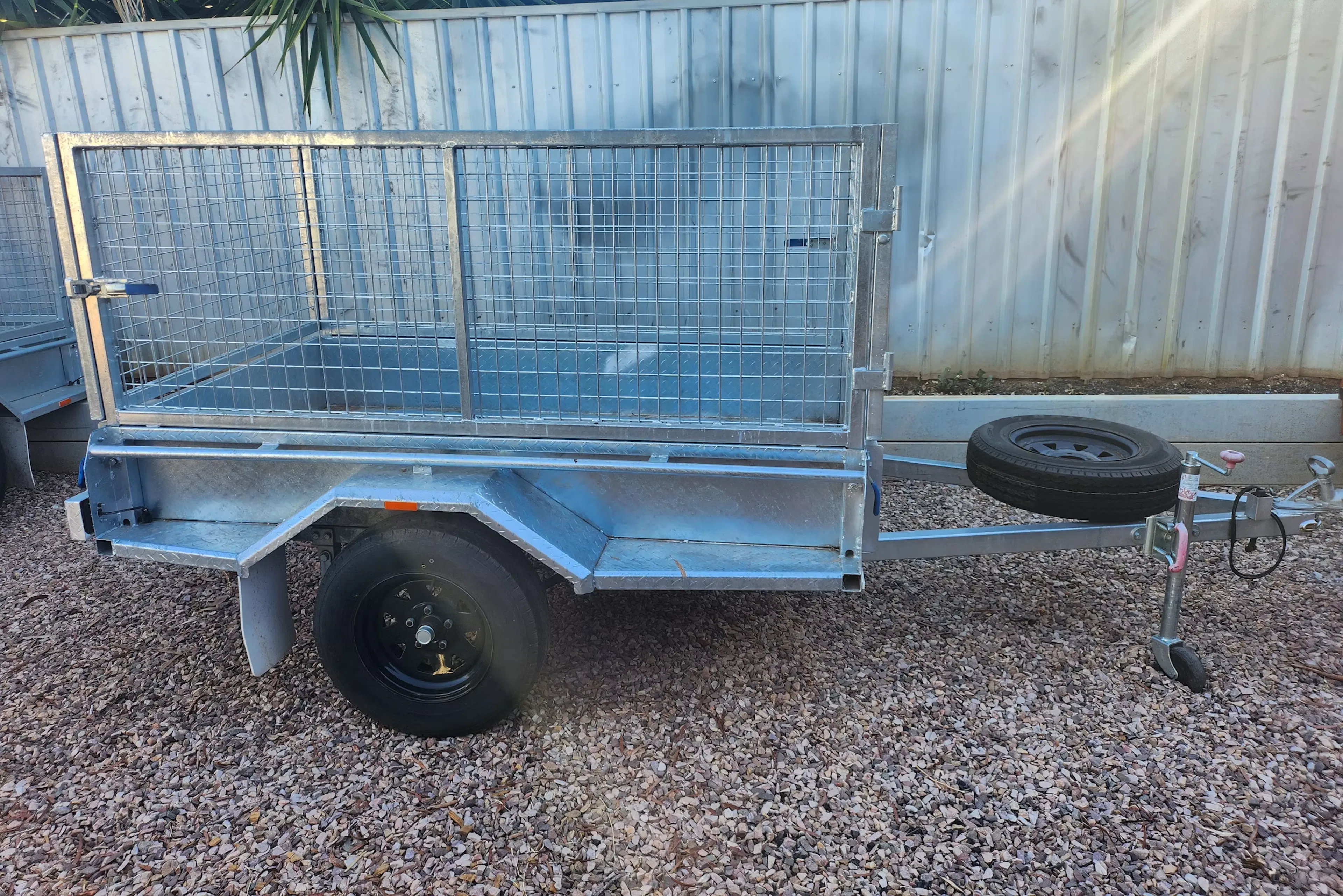 A vehicle trailer, cage style, parked on gravel