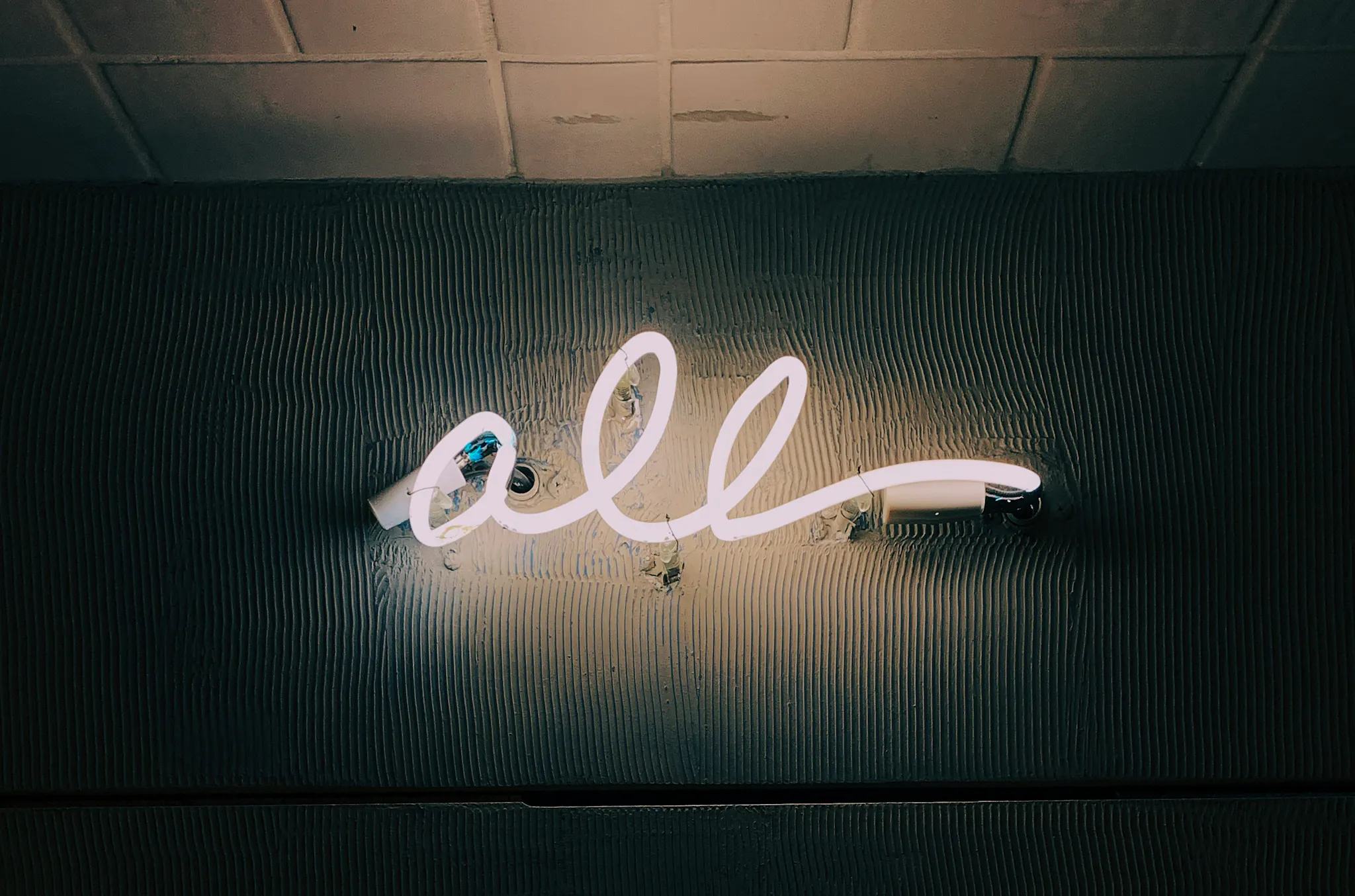 A wall lit up by a neon sign that says "all".