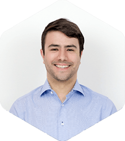 Luis is smiling widely at the camera. He has a light-blue shirt on with the top-most button open for a relaxed vibe.