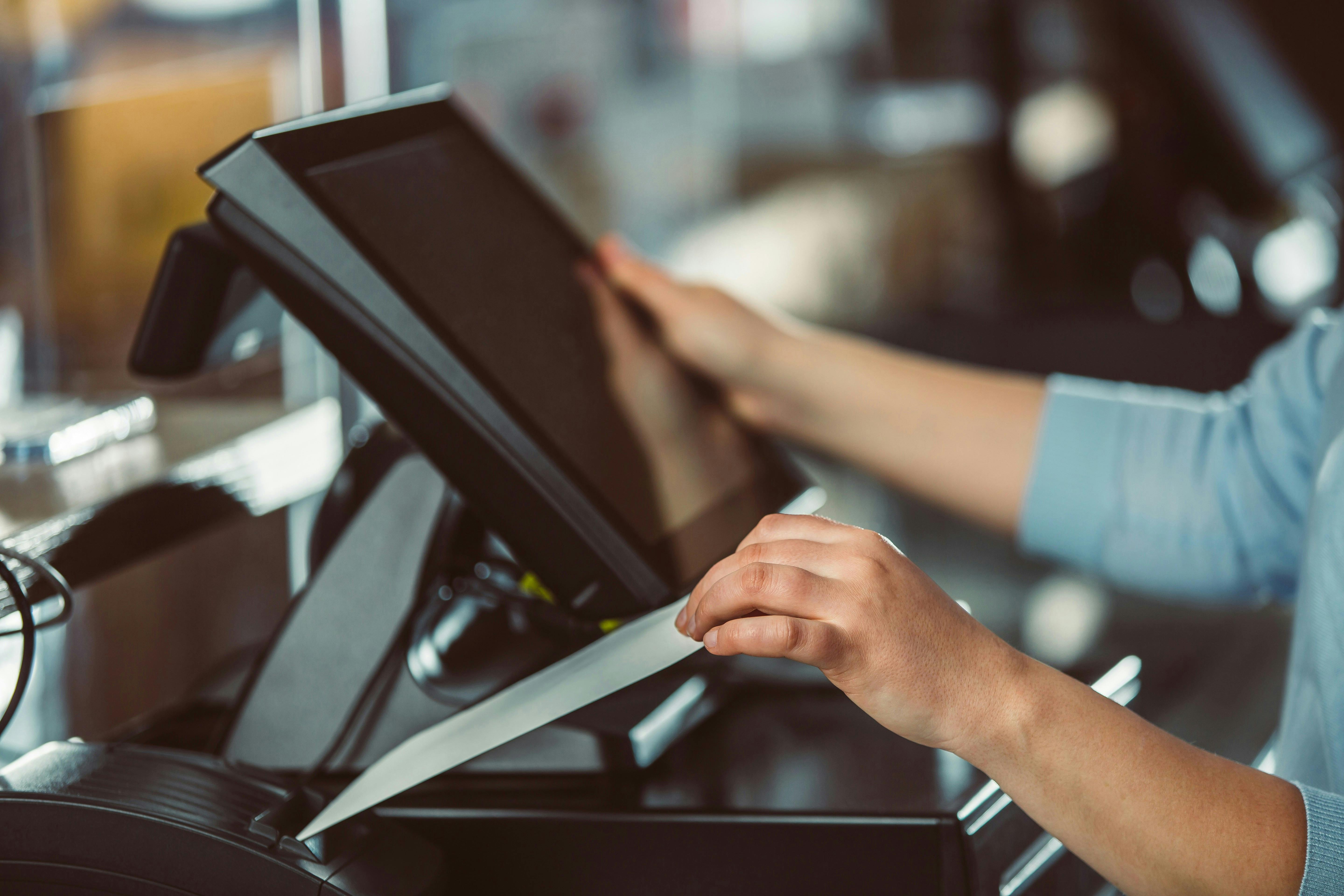 Store checkout machine with a person holding the screen with one hand and a receipt with the other.