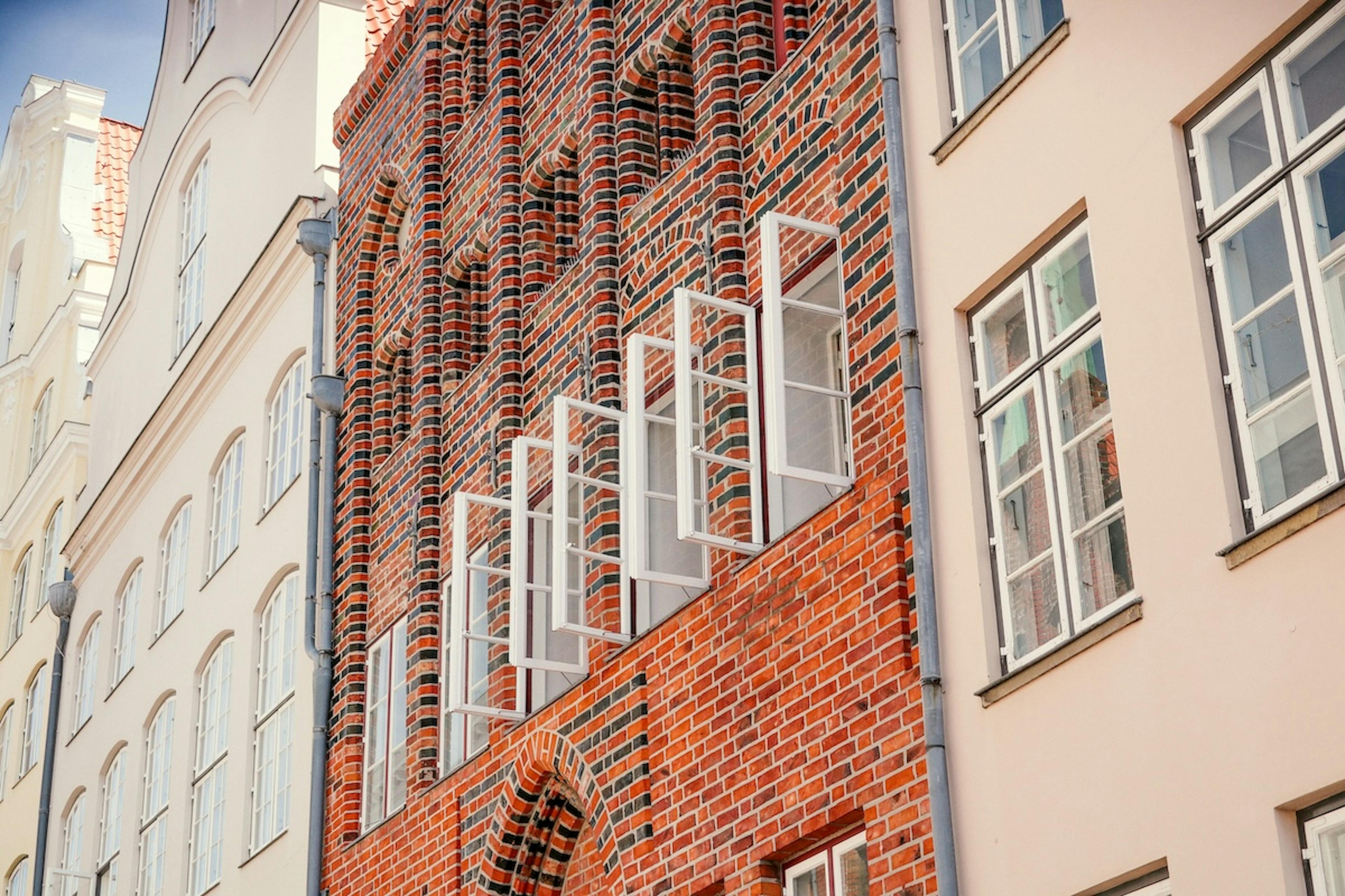A red brick building with white windows and shutters open next to two-beige-colored buildings with windows closed.