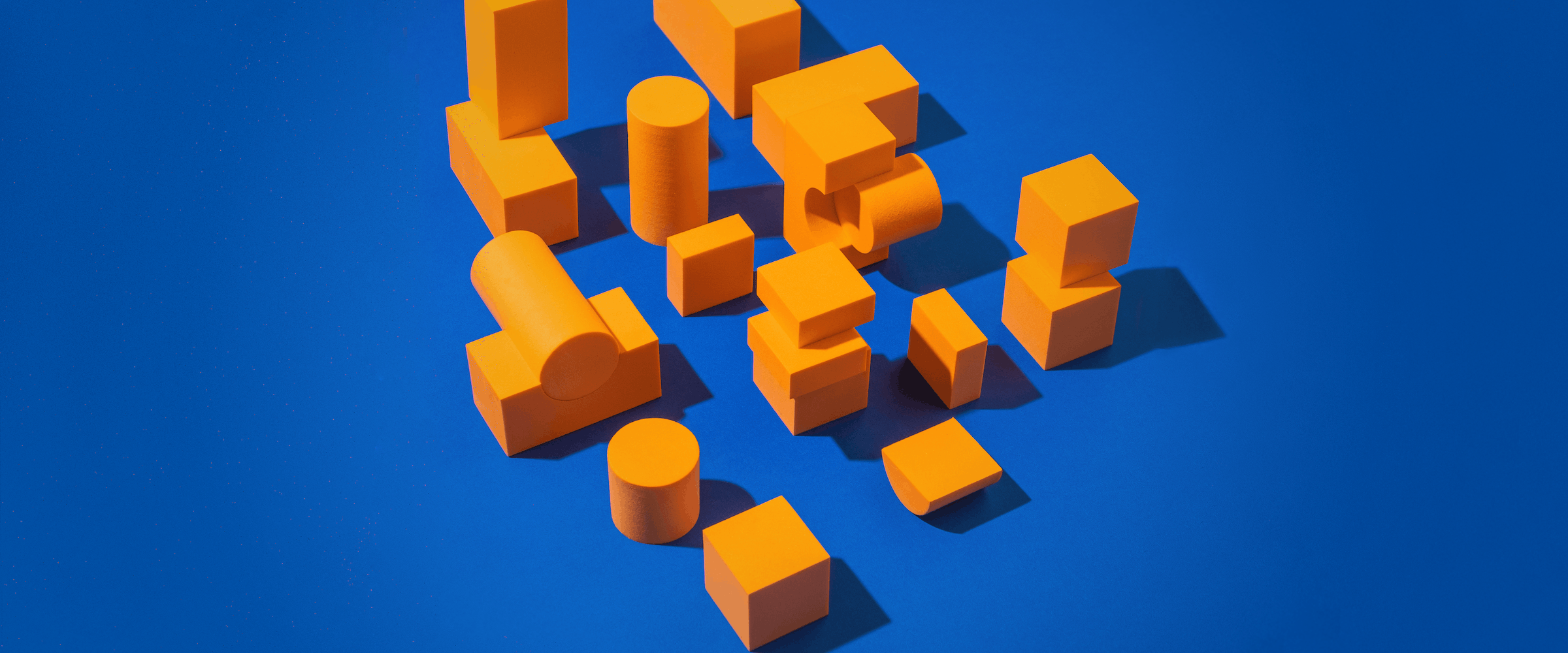 Bright orange geometric blocks of different shapes and sizes arranged on a bright blue background.