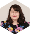 Amanda has dark, medium-lengthed brown hair, glasses, and a black floral shirt. She is smiling at the camera.