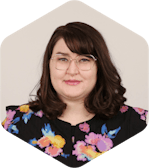 Amanda has dark, medium-lengthed brown hair, glasses, and a black floral shirt. She is smiling at the camera.