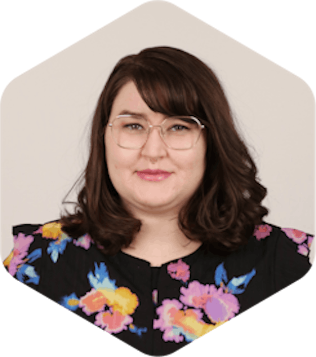 Amanda has dark, medium-lengthed brown hair, glasses, and a black floral shirt. She is smiling at the camera.