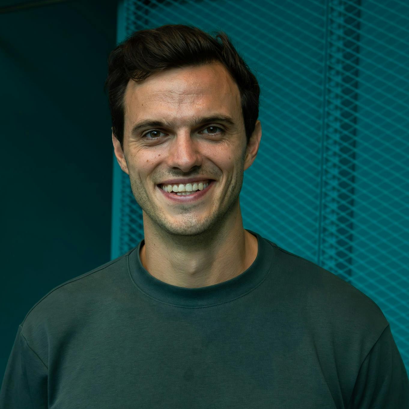 Headshot of socialbnb co-founder Nils Lohmann in a green t-shirt, smiling, against a turquoise textured background.