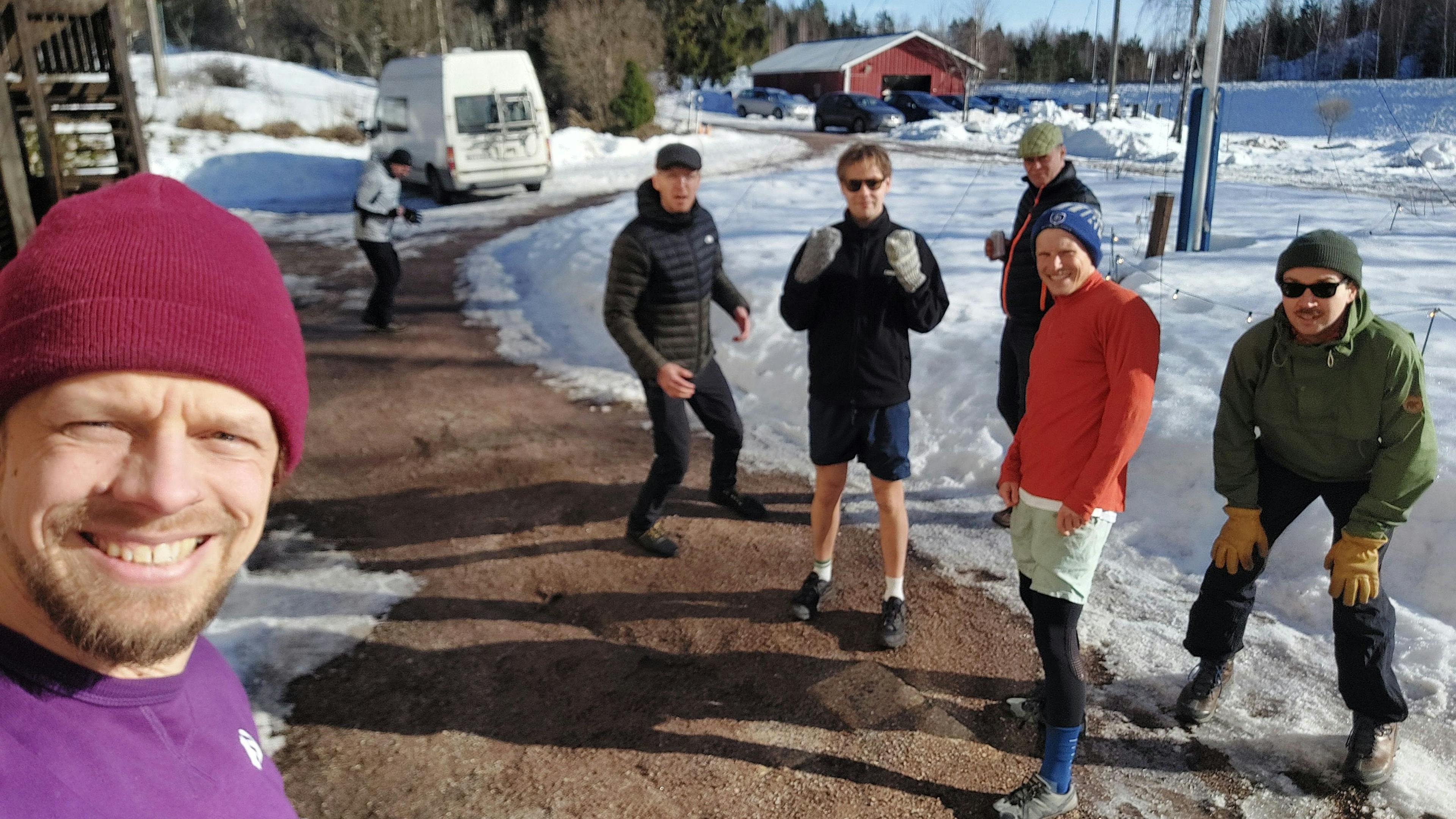 Antti takes a selfie with Sjoerd, Aleksi, Tom, Hannu and Vesa behind him outdoors in winter, wearing running clothes on a snowy path.