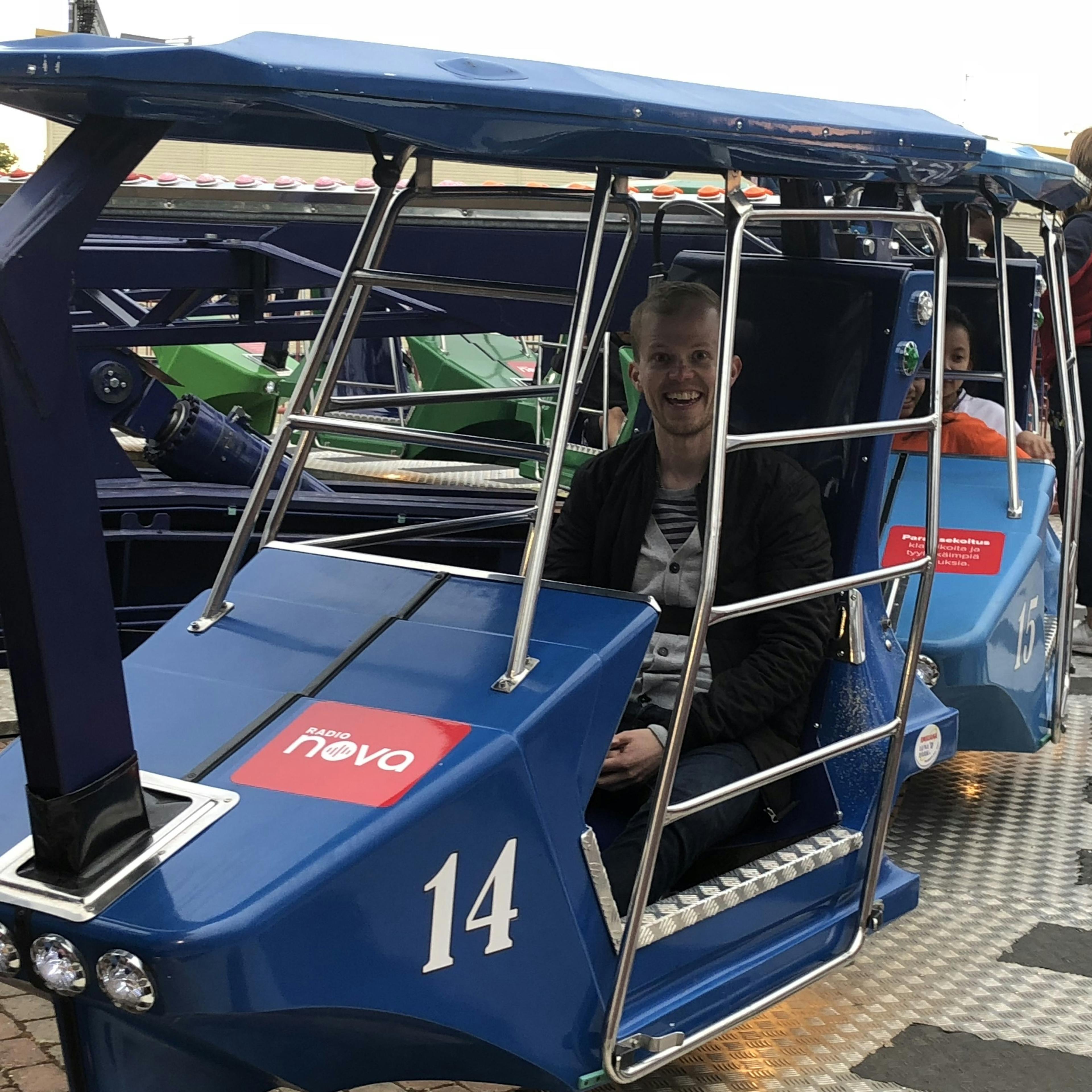 Juho seated in a blue amusement ride car at an amusement park.