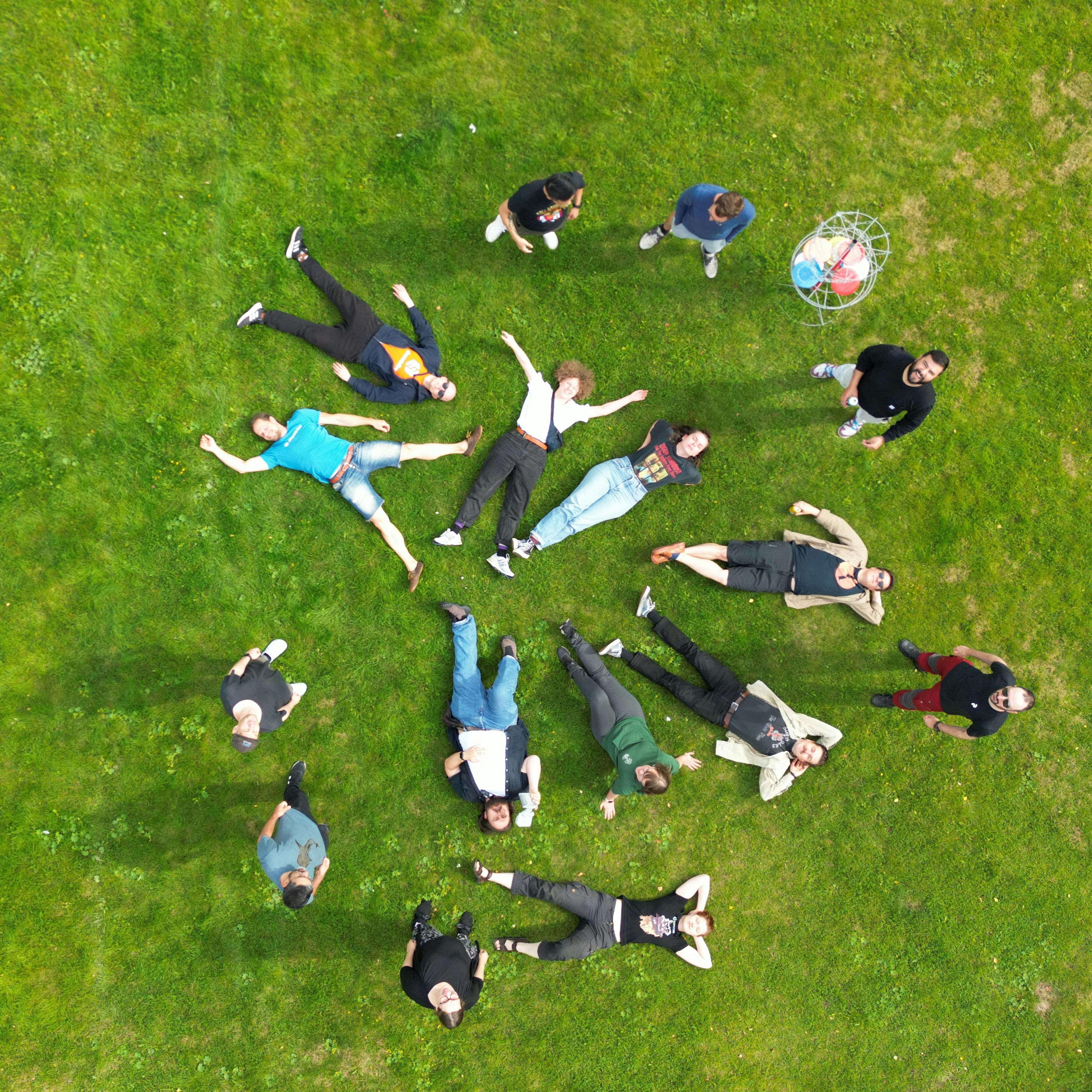 Sharetribe team lying on green grass in a circle, photographed from above.