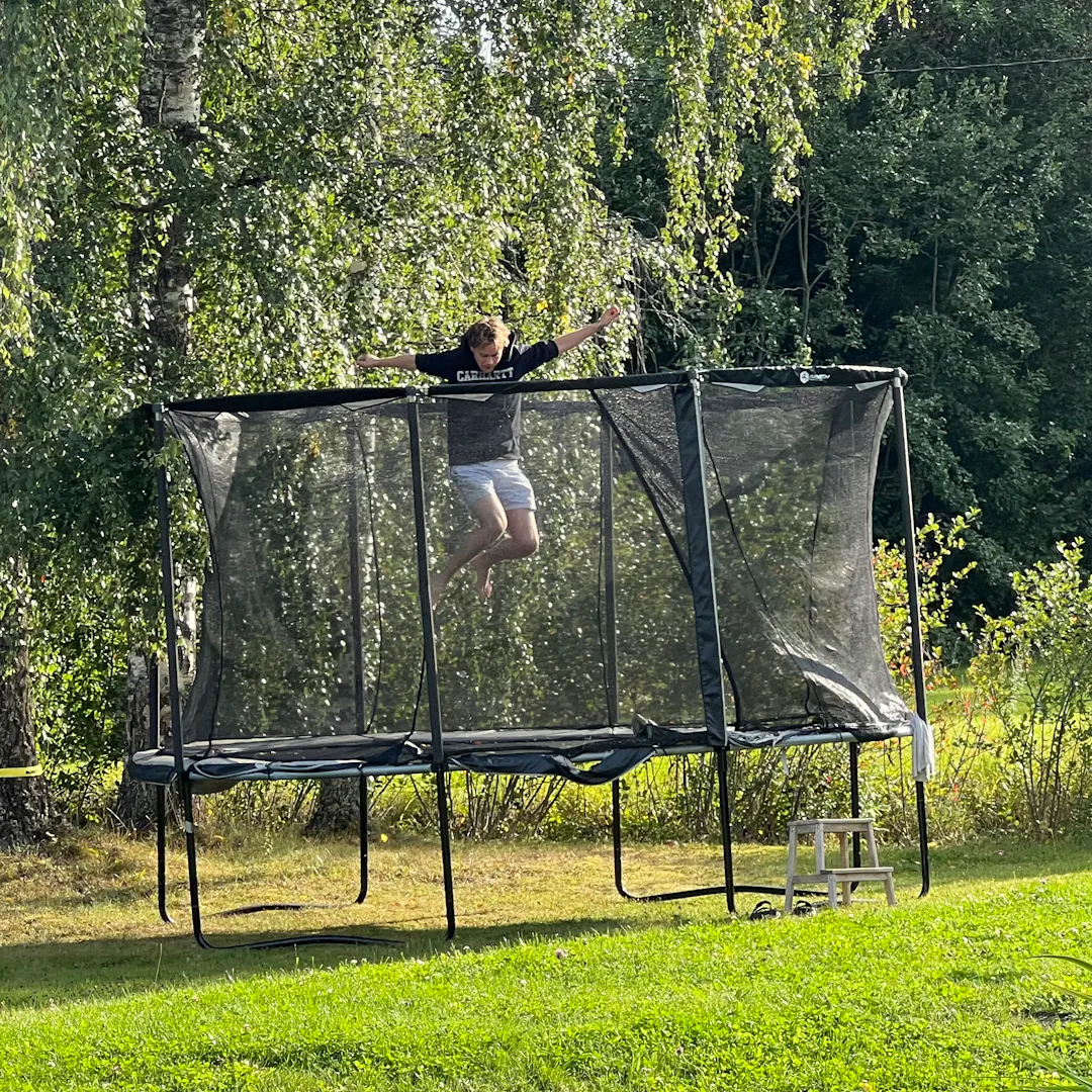 Aleksi jumping on a trampoline in a green garden on a warm summer day.