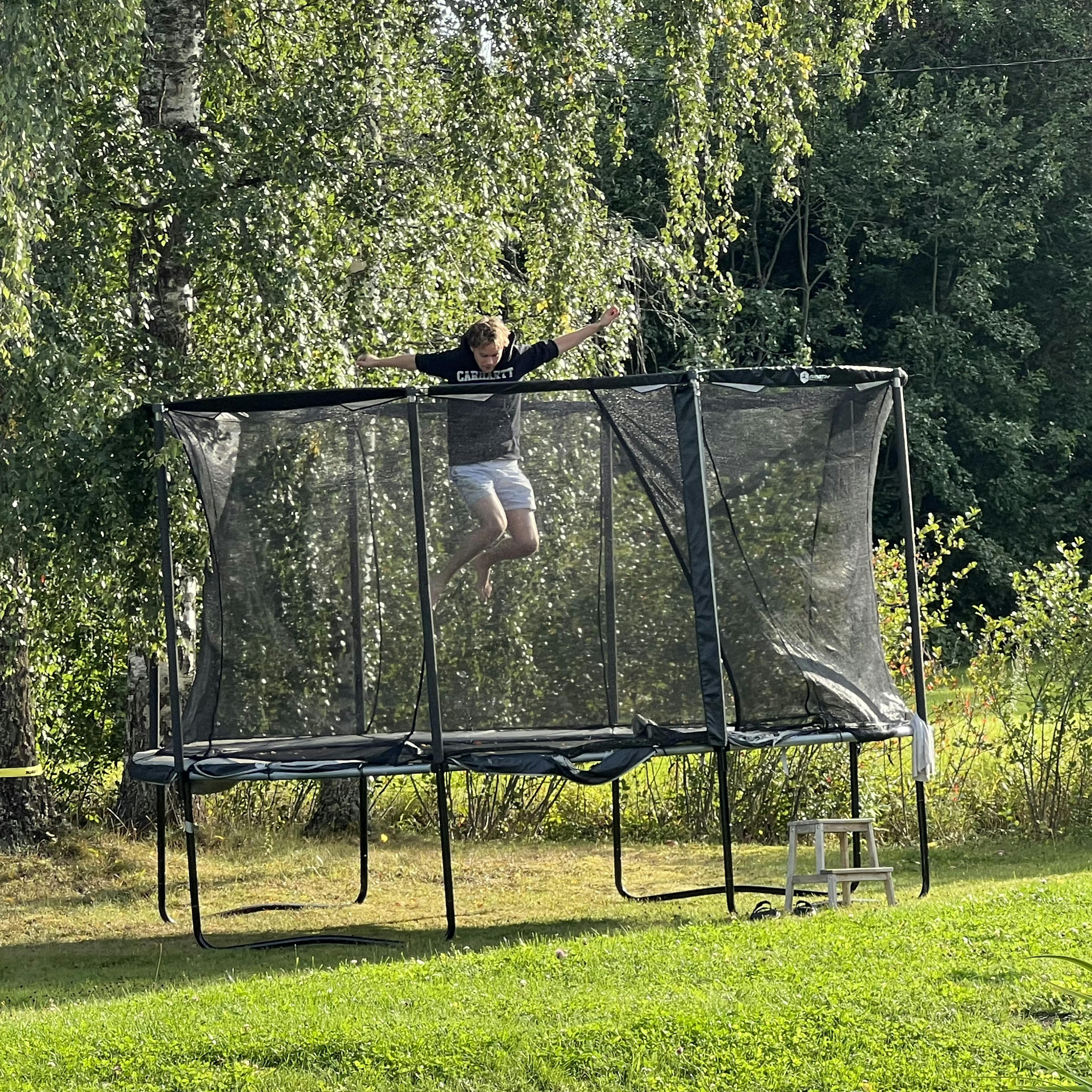 Aleksi jumping on a trampoline in a green garden on a warm summer day.