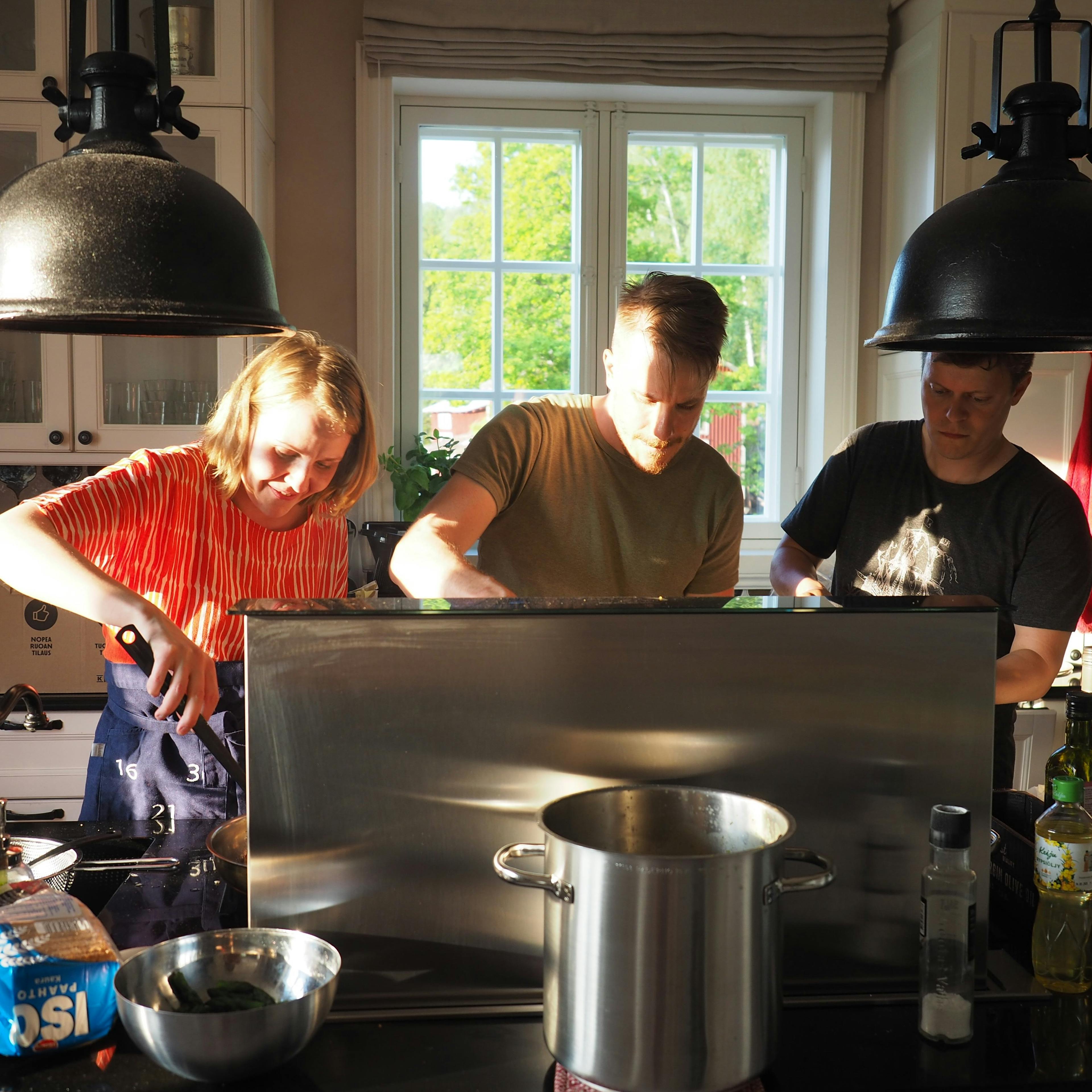 Three people cooking together in a bright kitchen, preparing food at a stovetop