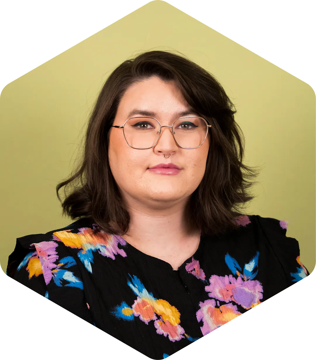 A headshot of Amanda wearing floral shirt on a green background, gently smiling at the camera. 