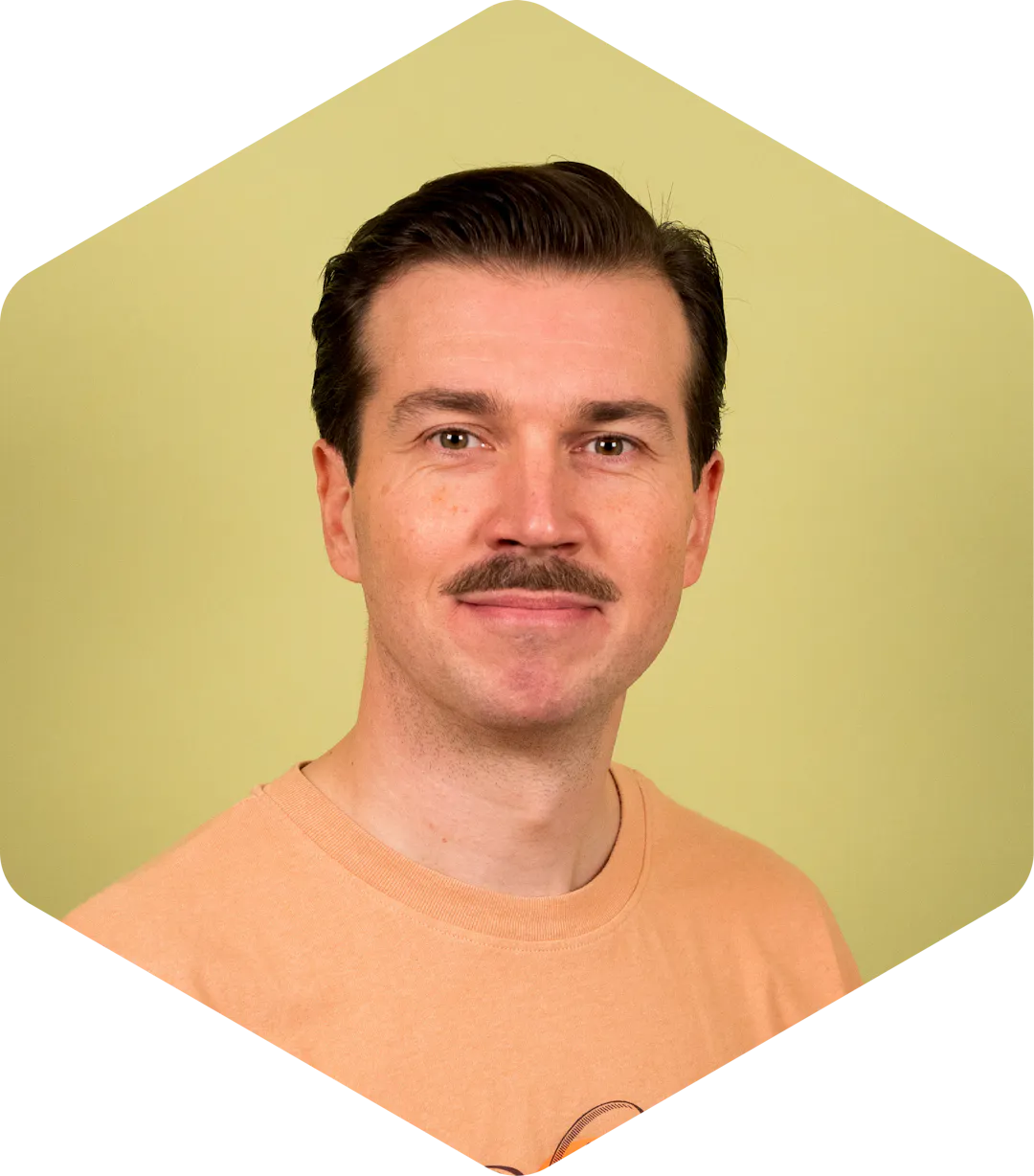 Hannu wearing an orange T-shirt, facing the camera on a light green background.