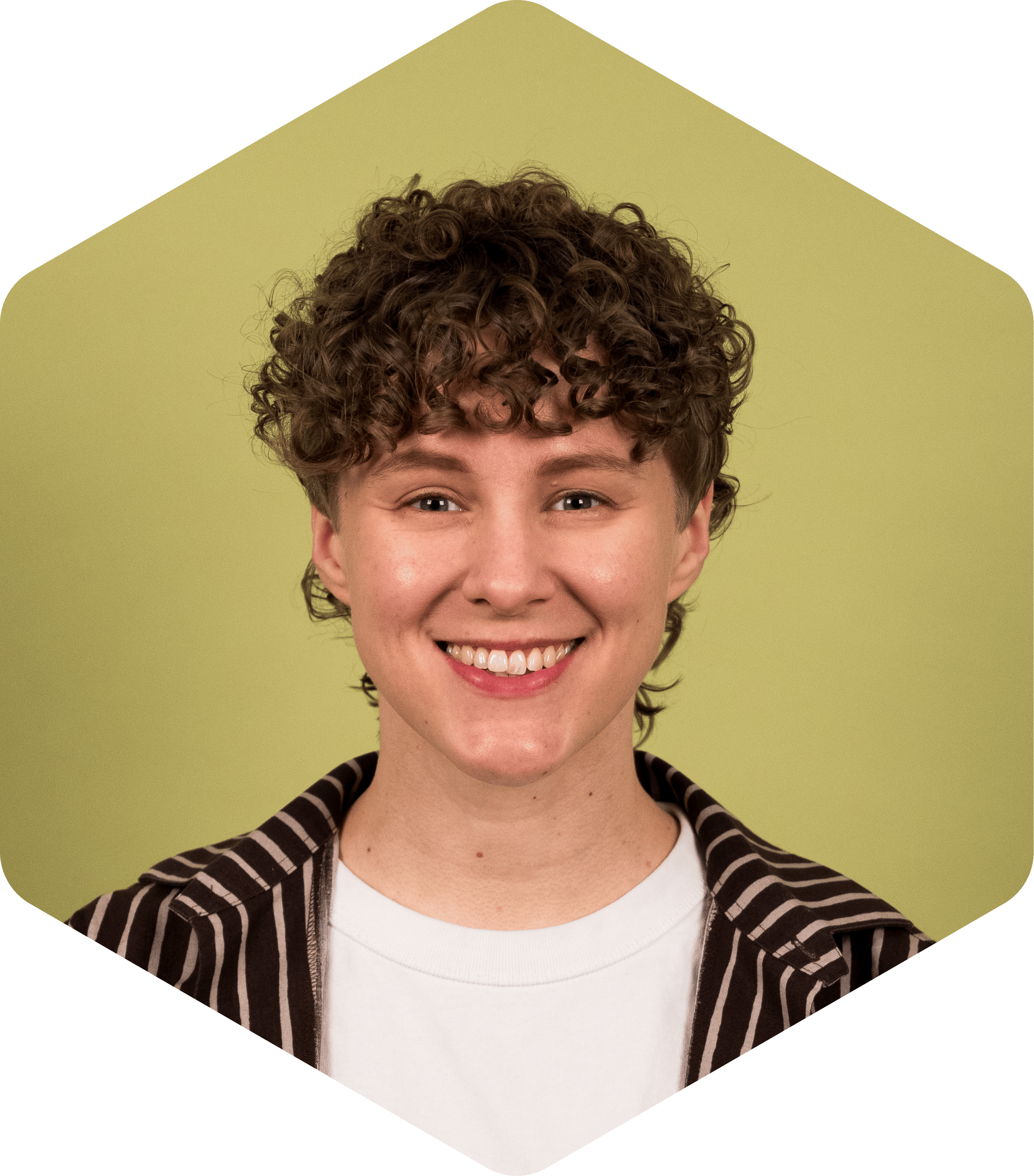 Katri is a white woman with short, curly hair and she's smiling facing the camera. She's wearing a brown, striped Marimekko shirt over a white tee.