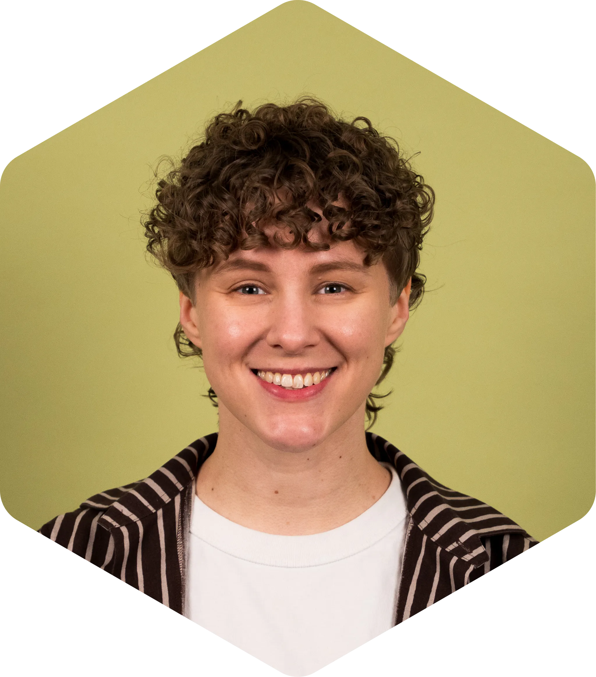 Katri is a white woman with short, curly hair and she's smiling facing the camera. She's wearing a brown, striped Marimekko shirt over a white tee.
