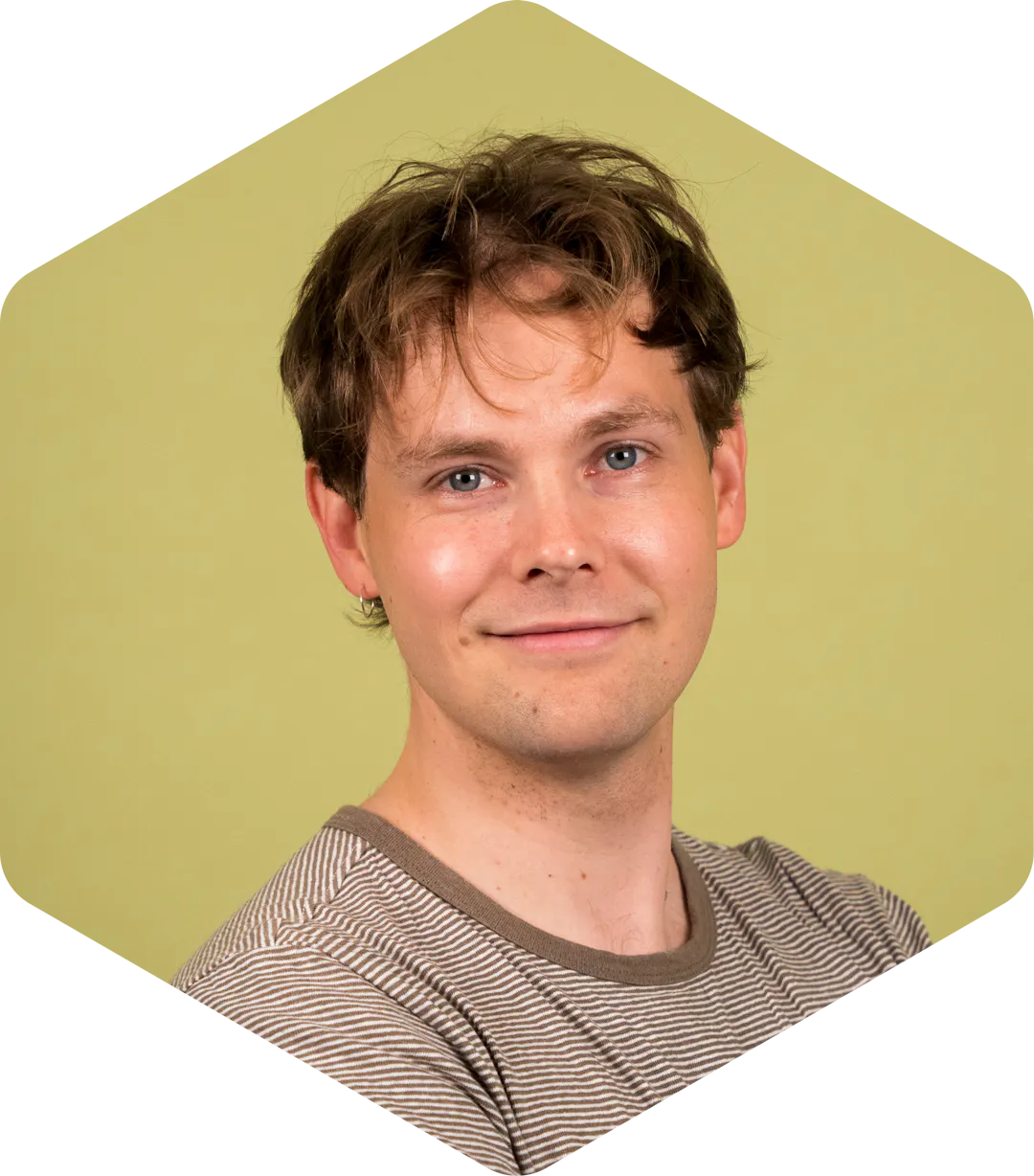 Aleksi smiling, wearing a striped shirt, against a light green background.