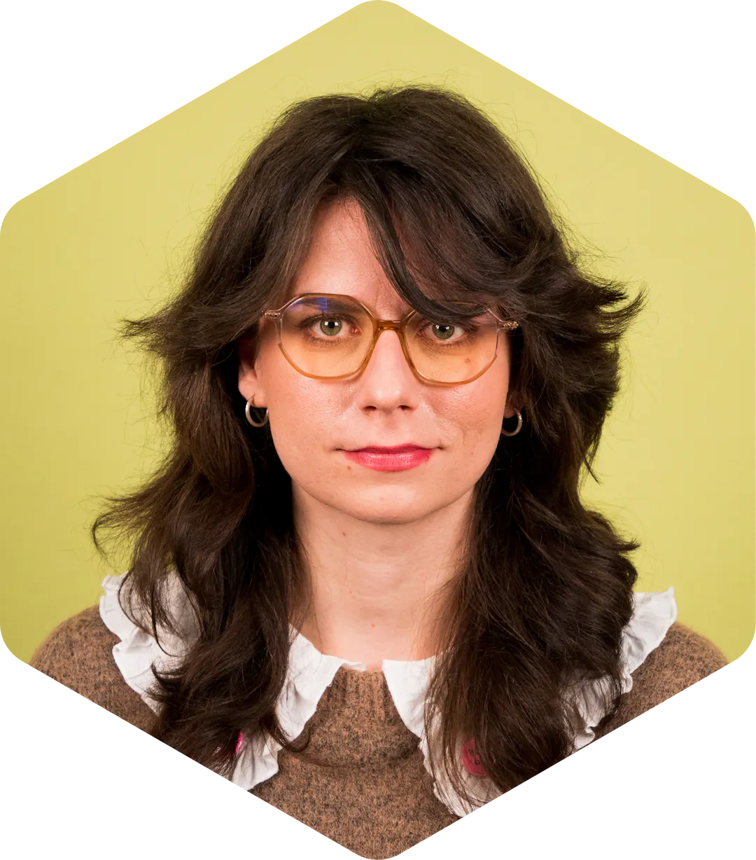Kinga facing the camera, wearing glasses, on a light green background.