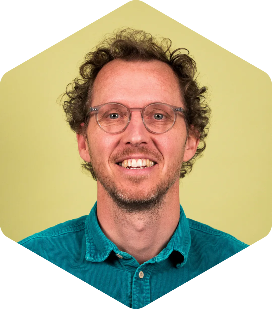 Sjoerd smiling, wearing a teal button-down shirt on a light green background.