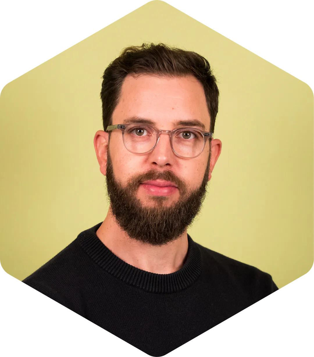 Thomas wearing glasses and a navy sweater on a light green background.