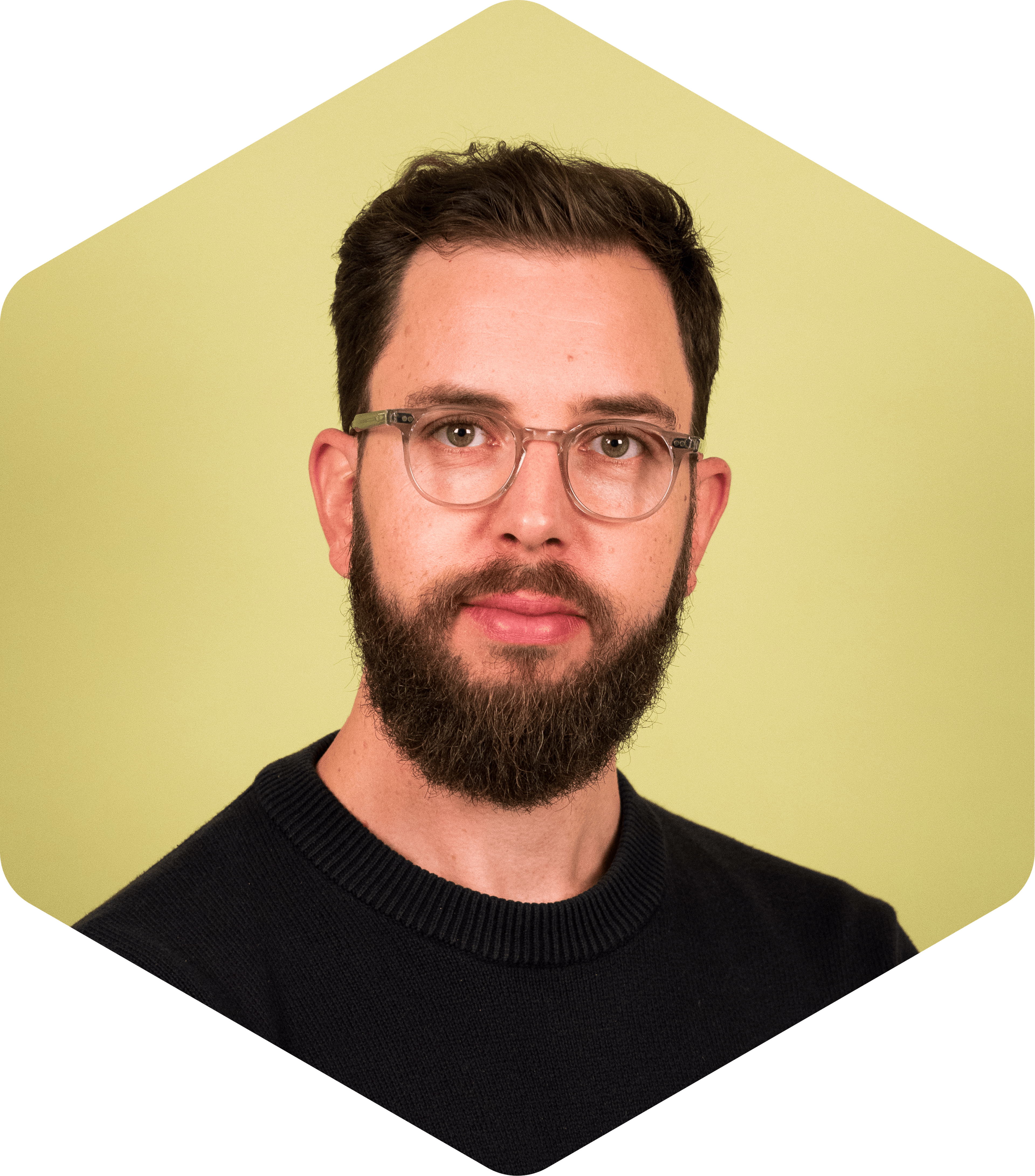 Thomas wearing glasses and a navy sweater on a light green background.