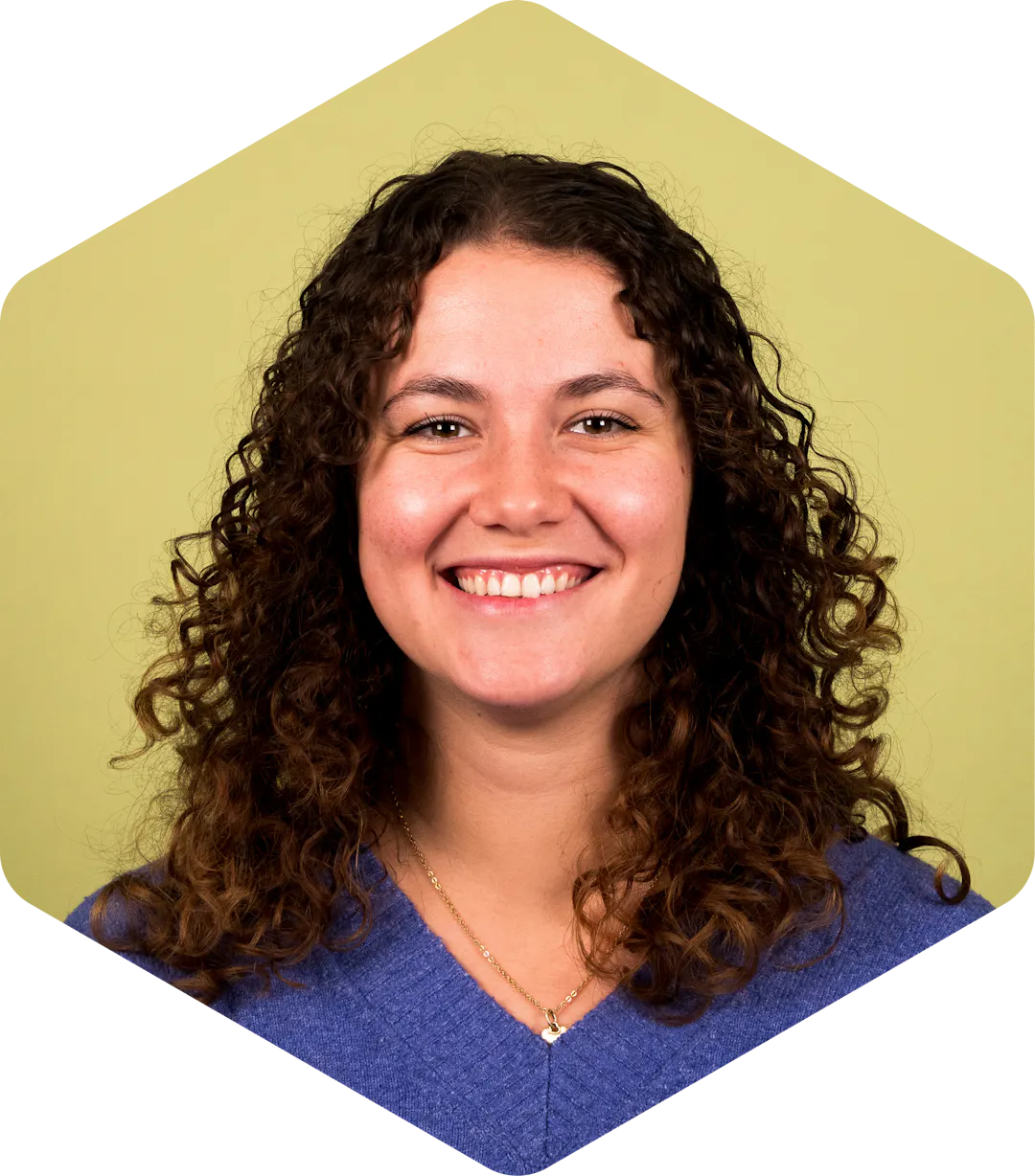 Portrait of Valeria smiling warmly at the camera against a light green background.