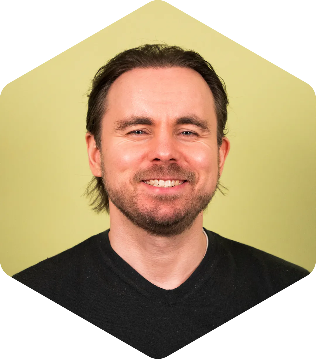 Portrait of Vesa smiling gently at the camera, wearing a black shirt on a light green background.