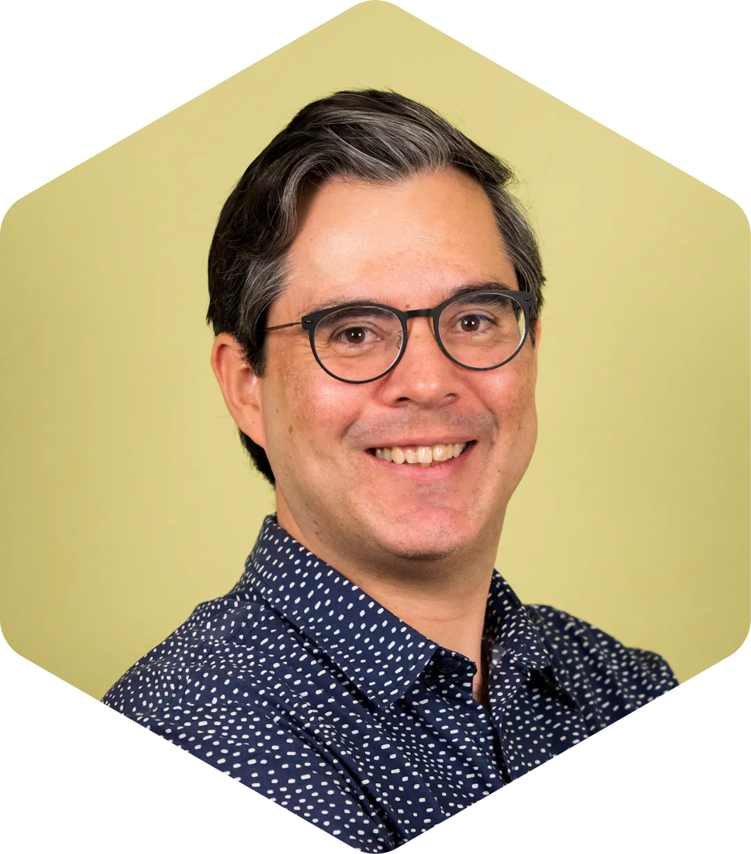 Portrait of Walter smiling gently at the camera, wearing glasses and a patterned shirt against a light green background.