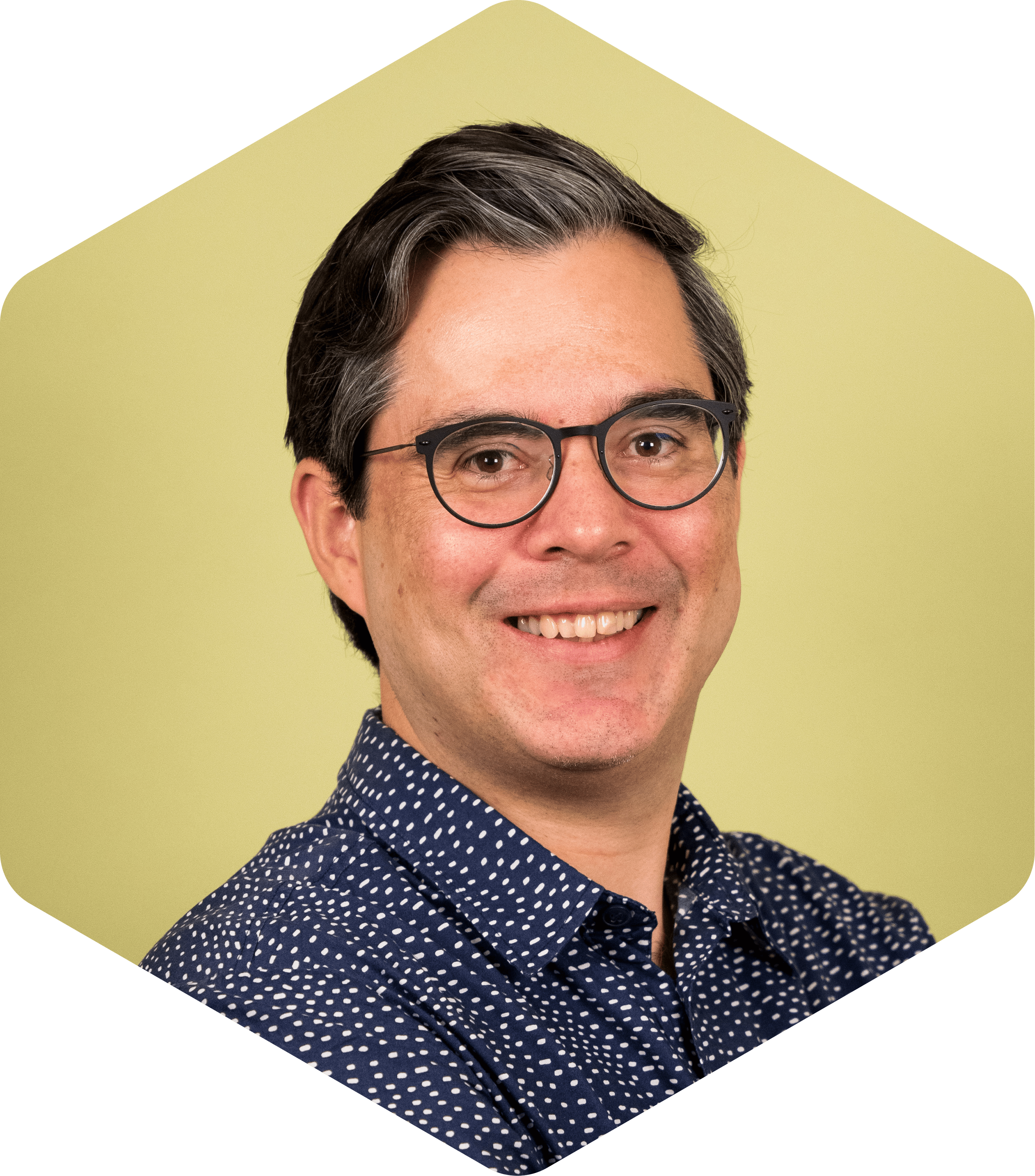 Portrait of Walter smiling gently at the camera, wearing glasses and a patterned shirt against a light green background.