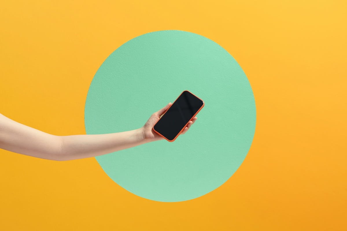 Hand holding smartphone with empty screen on light background.