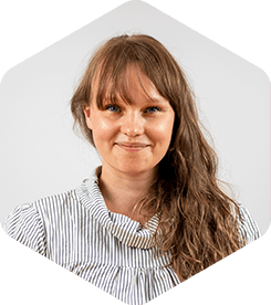 Sari has long light-brown hair and bangs and she's wearing a striped shirt with a slightly puffy collar. She's smiling at the camera.