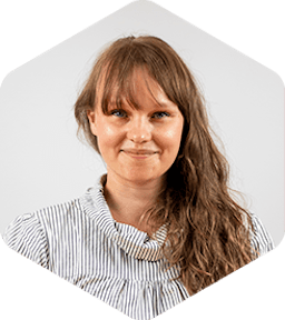 Sari has long light-brown hair and bangs and she's wearing a striped shirt with a slightly puffy collar. She's smiling at the camera.