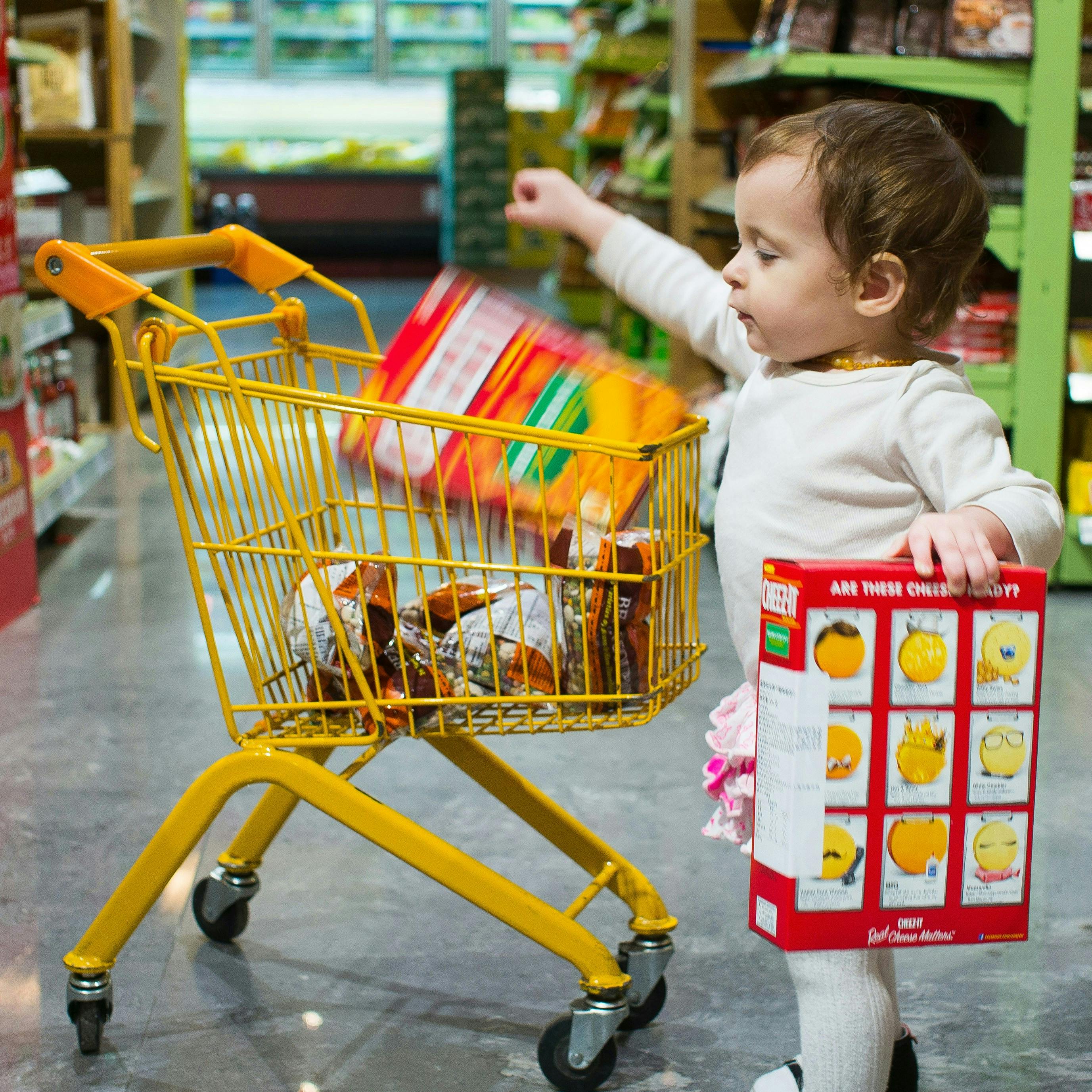 A child adding grocery items to a small yellow shopping cart.