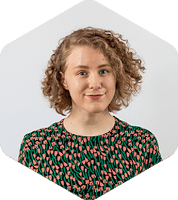 Katri is white woman with curly dark blonde hair. She's wearing a shirt with salmon pink and green flowers.