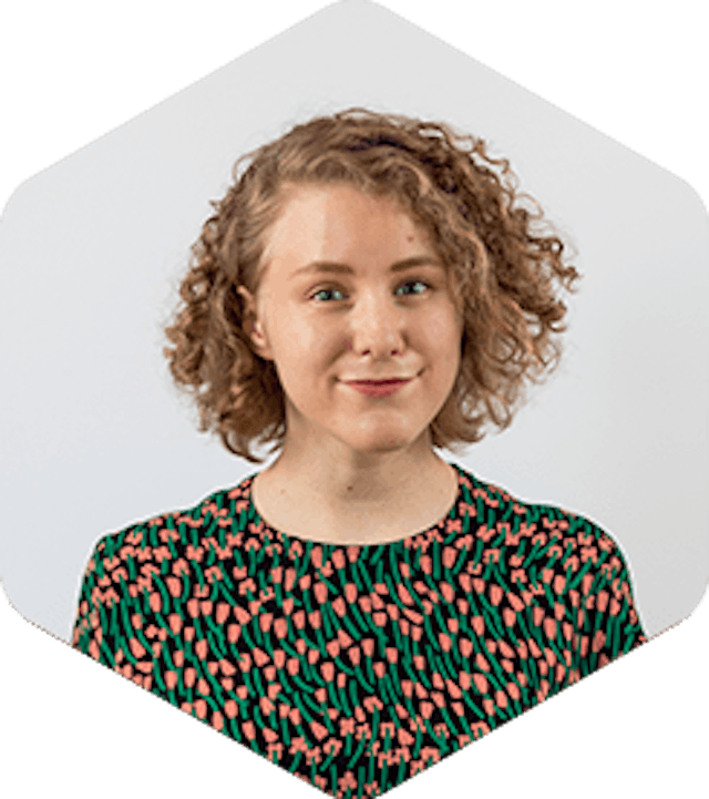 Katri is white woman with curly dark blonde hair. She's wearing a shirt with salmon pink and green flowers.